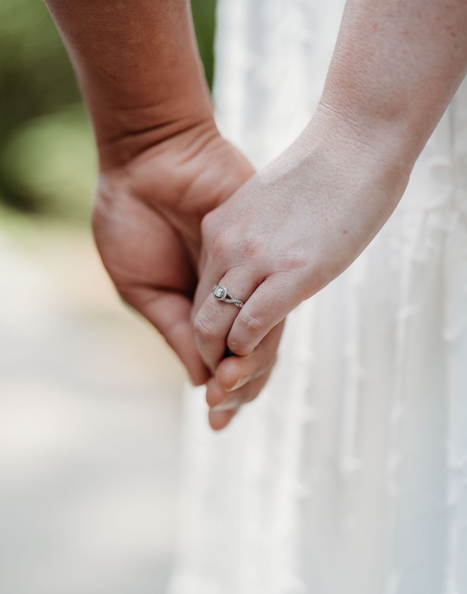 Close-up of clasped hands with a delicate engagement ring, showcasing an intimate wedding moment against a soft background.