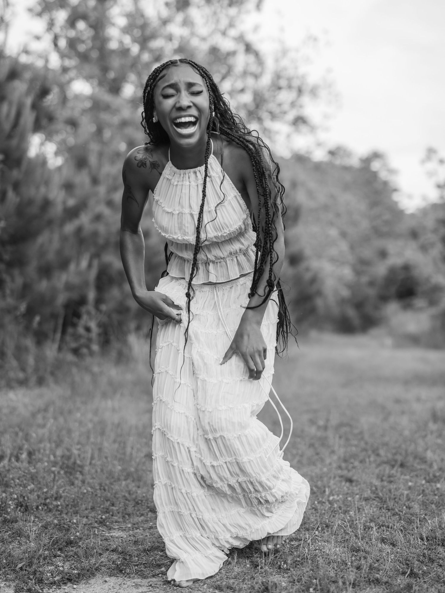 A joyful moment captured in black and white as a person in a white flowing dress dances freely in a grassy field.