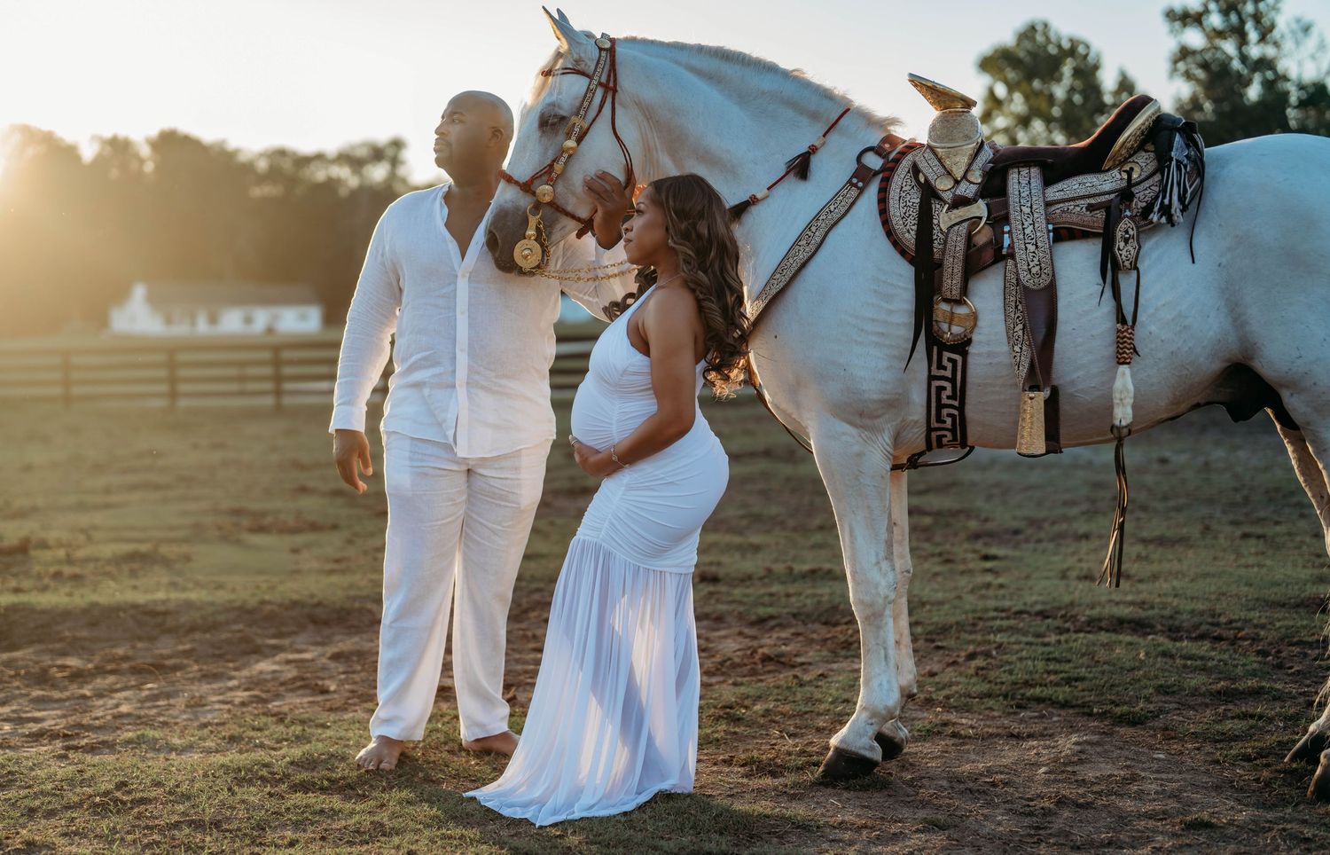 A romantic couple in white outfits poses with a horse in a sunlit field during golden hour.