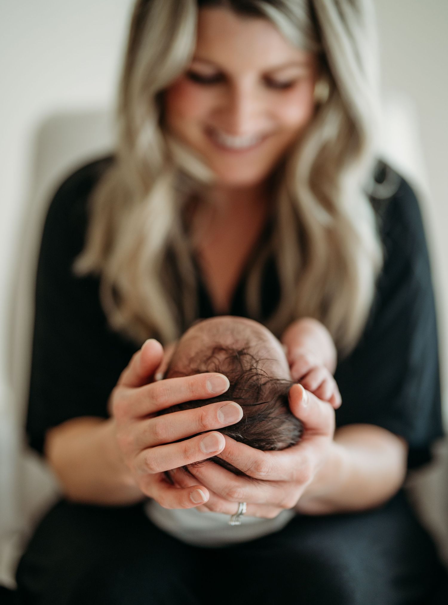 A woman in black holds a tiny sleeping newborn baby in her cupped hands through a series of intimate portraits.