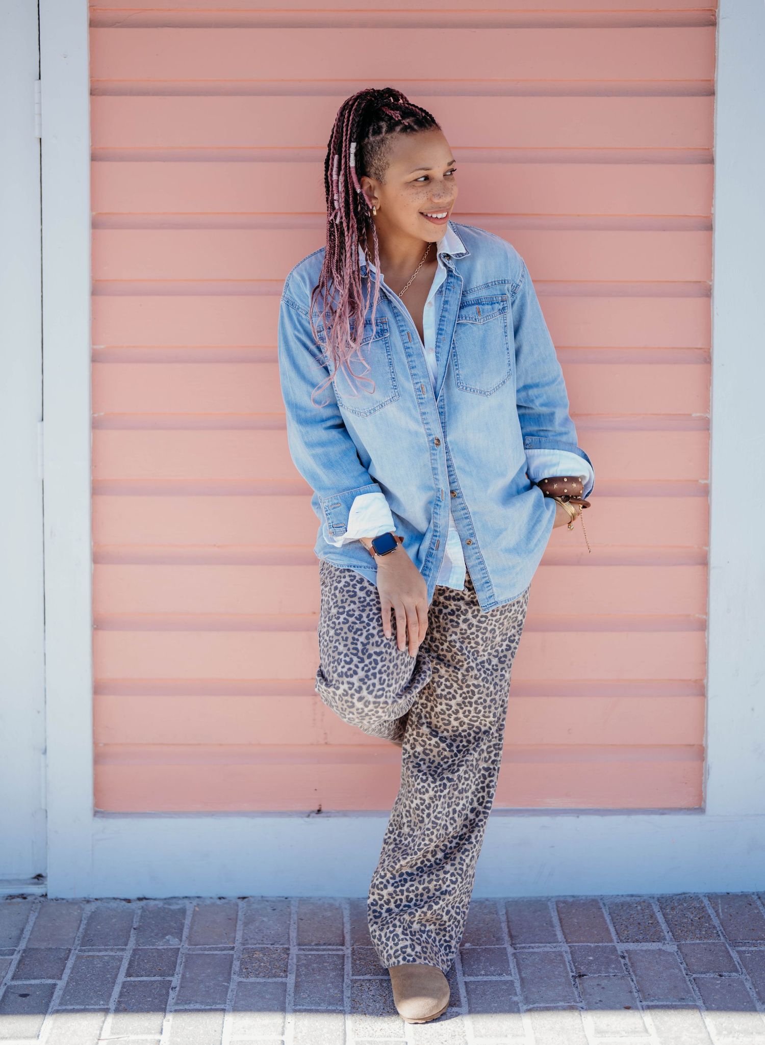 Stylish outfit featuring a light denim shirt paired with a leopard print skirt against a pink wall background.