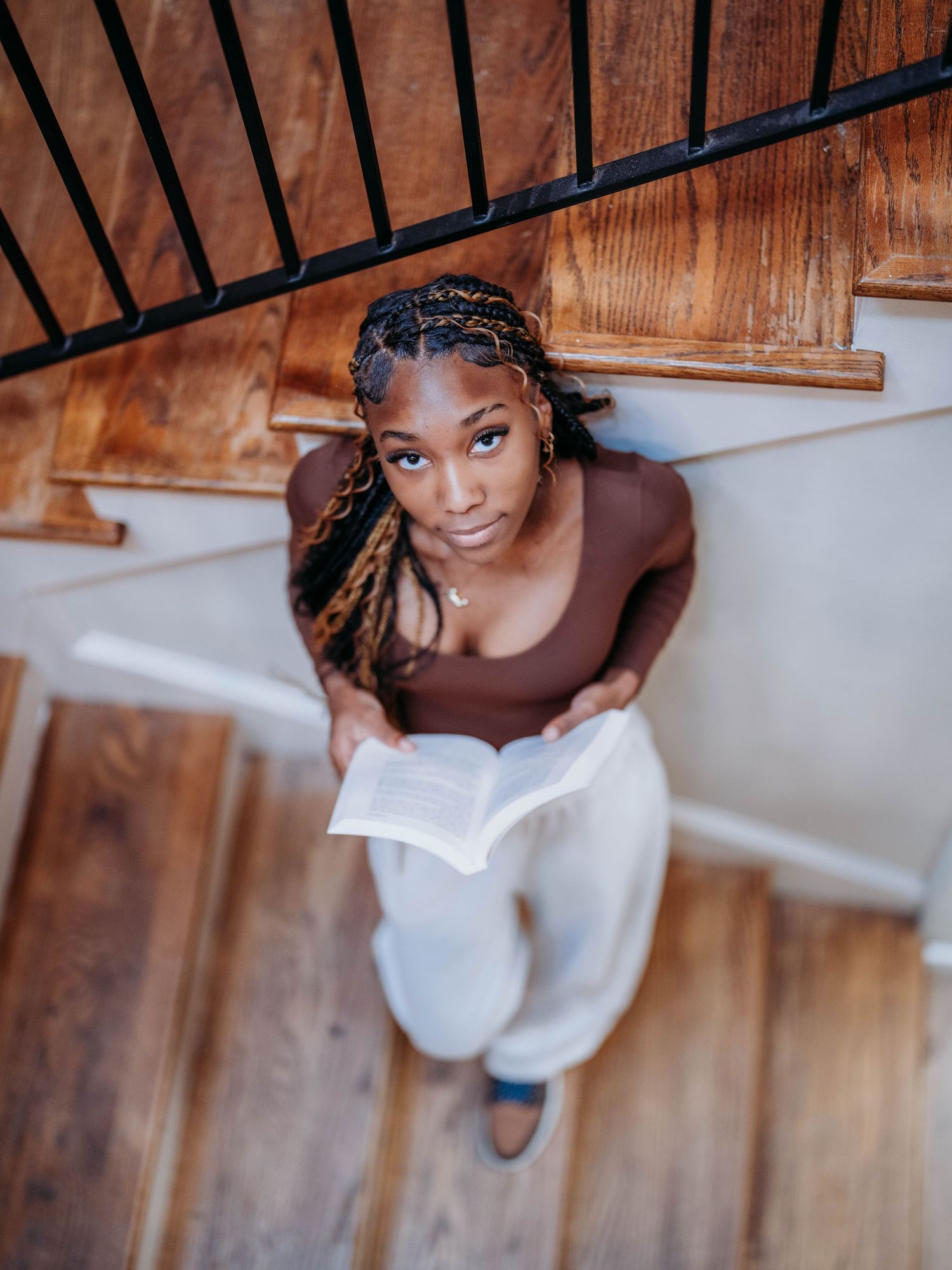 Person in white sweater sits on wooden stairs while looking up at camera with natural lighting.