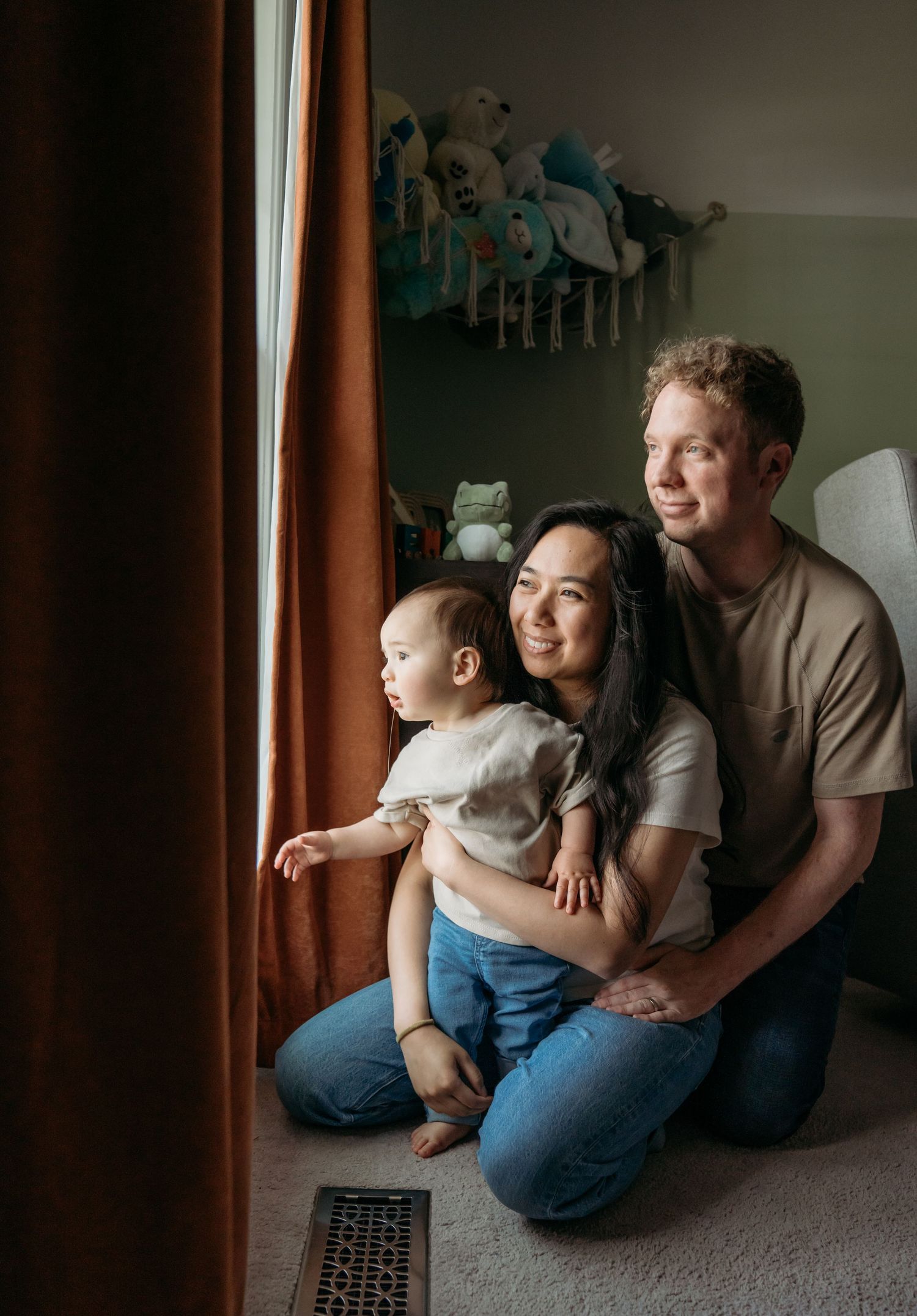 A family sits together by a window in a cozy room with natural lighting and brown curtains.