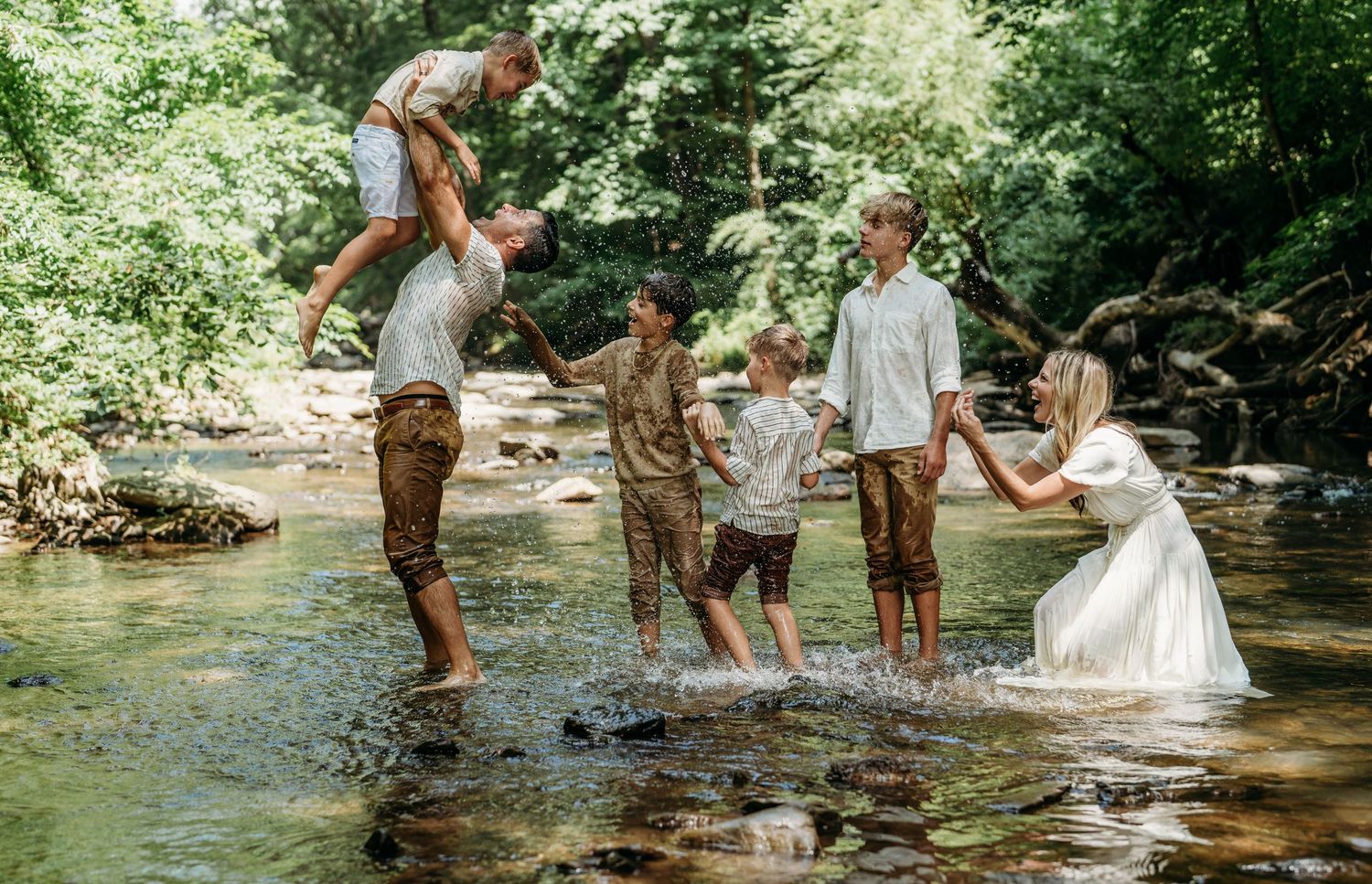 Joyful family moment captured while playing together in a sunlit forest stream.