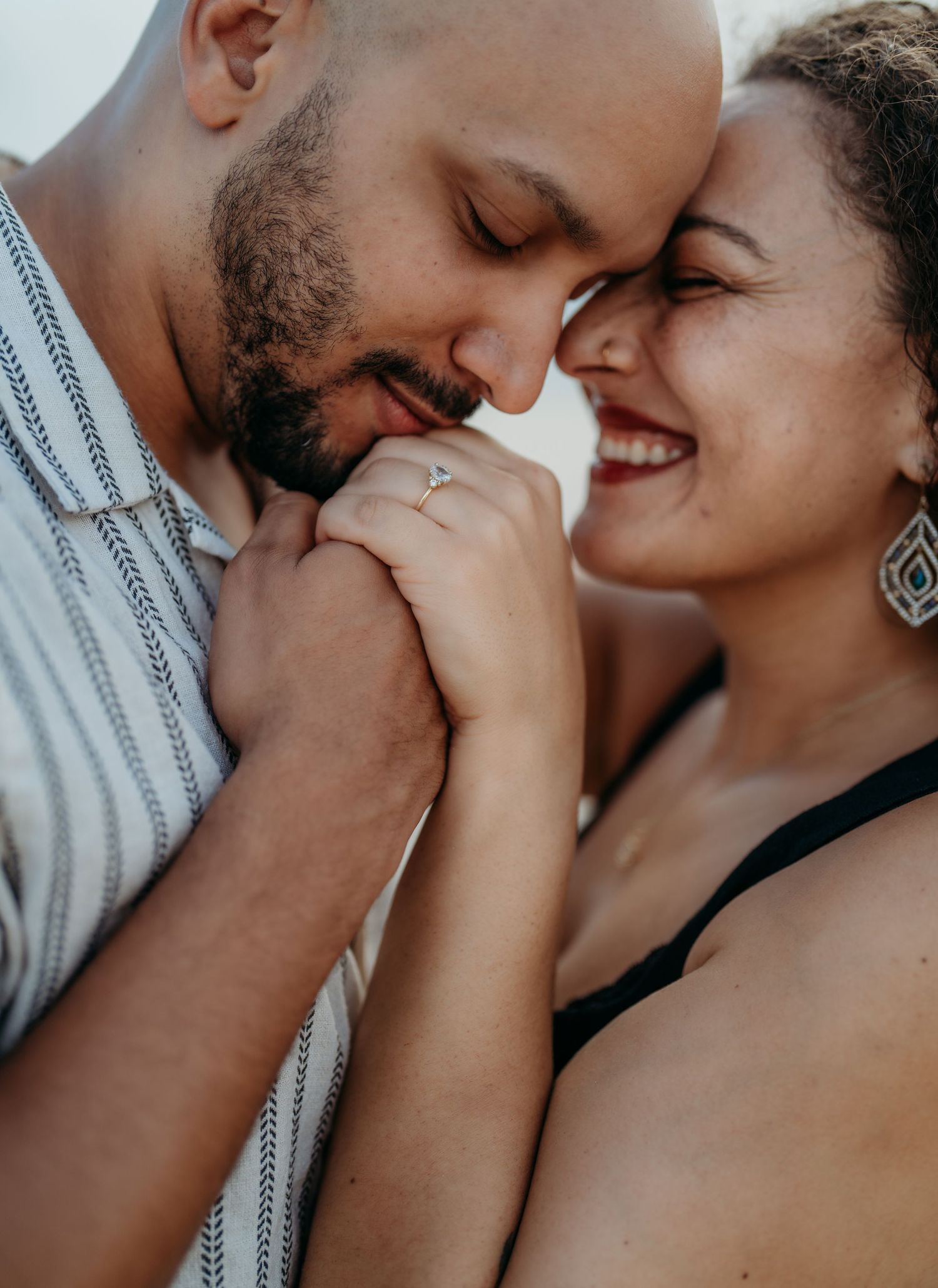 A romantic couple shares an intimate close-up moment with their faces touching tenderly against a light background.