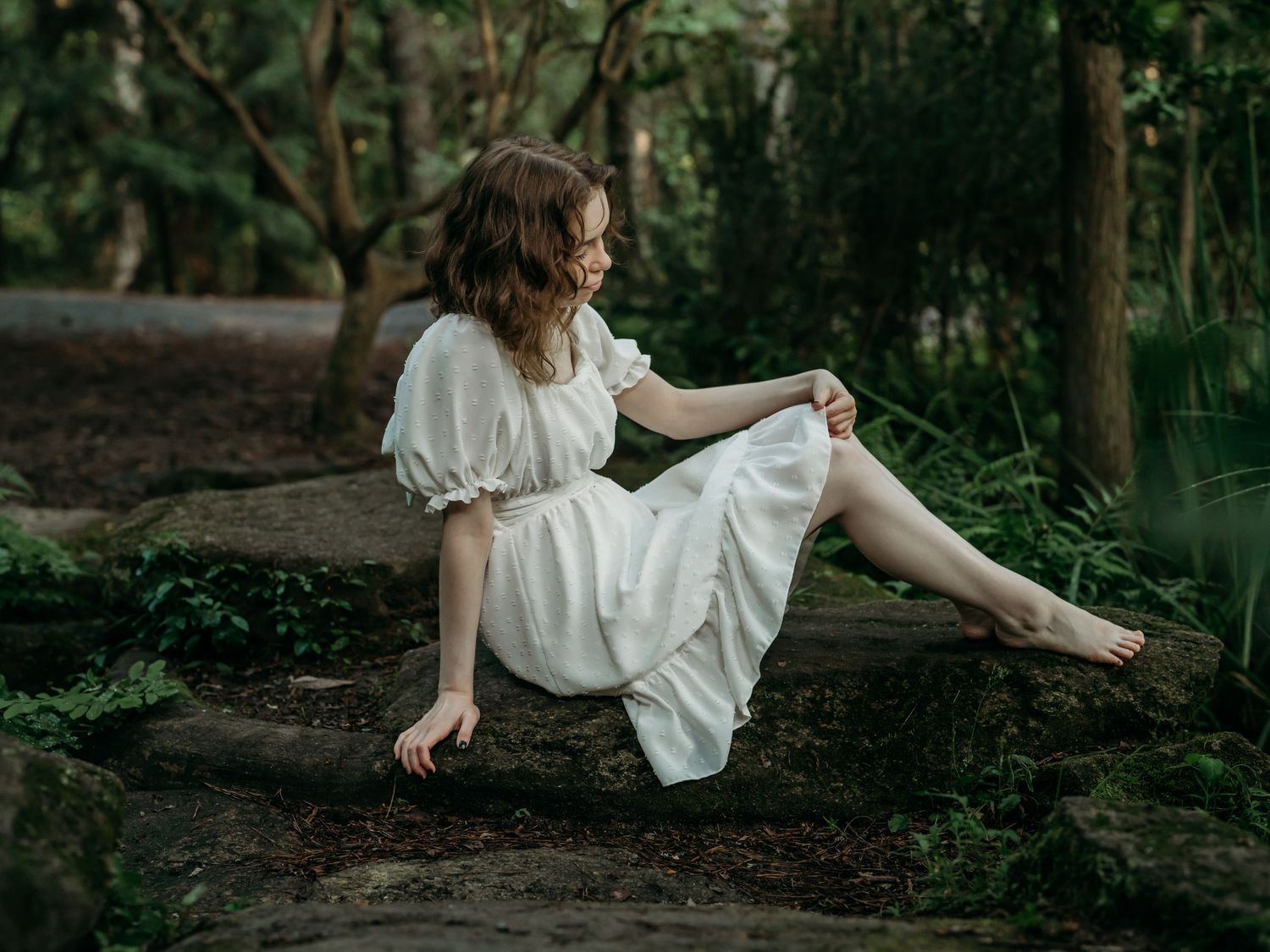 Person in white dress twirls gracefully through a mystical forest setting in a series of dreamy photographs.