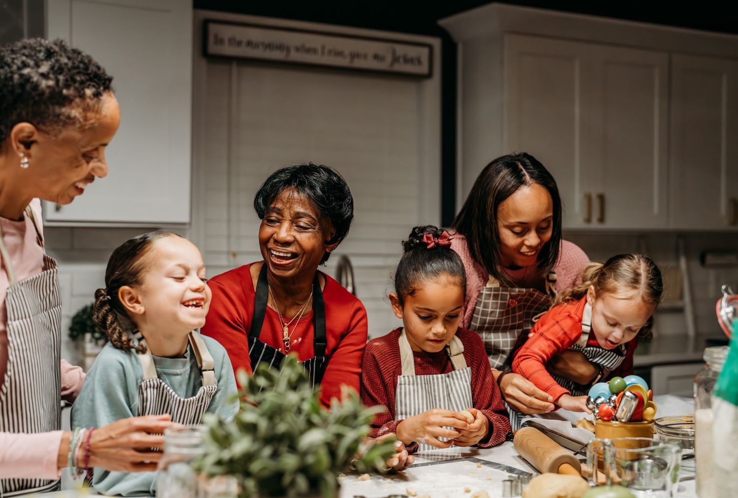Multi-generational family gathers around kitchen counter laughing and enjoying meal preparation time together.