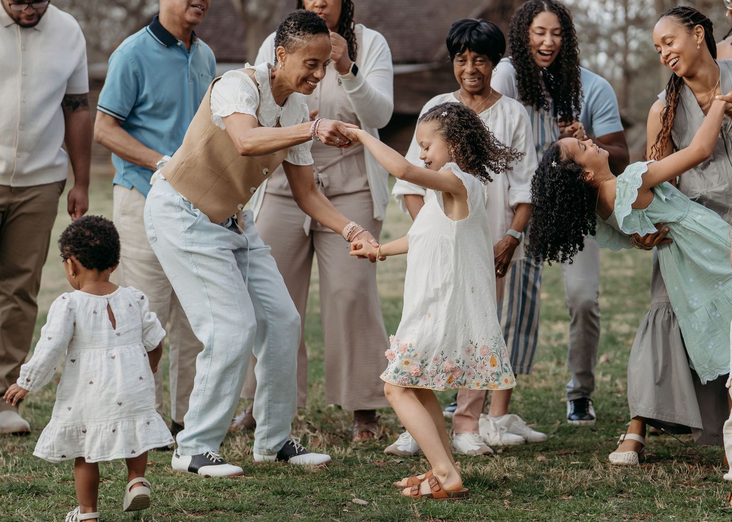 A family wearing coordinated white and blue outfits plays together in a grassy outdoor setting during a photo session.