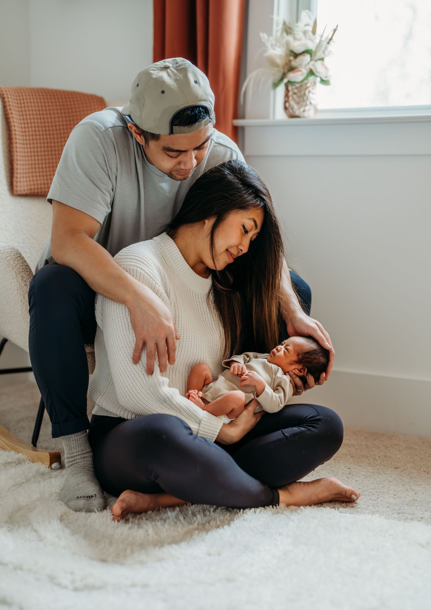 A tender moment unfolds as parents sit together on a plush white rug taking care of their newborn at home.