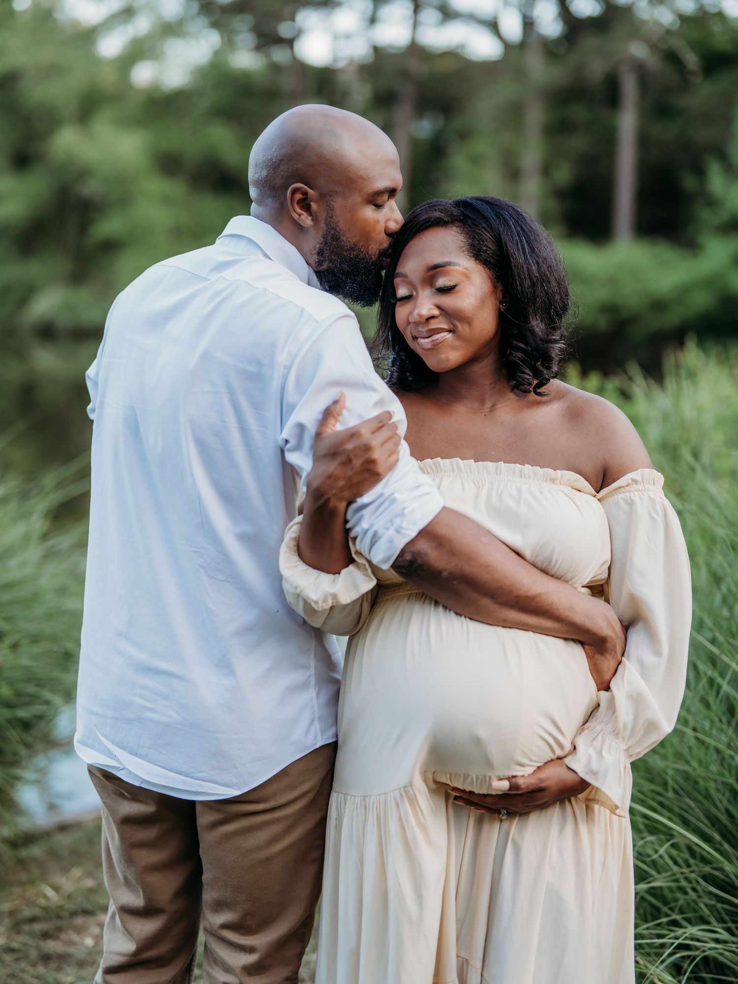 A romantic maternity portrait with couple embracing outdoors in natural setting.