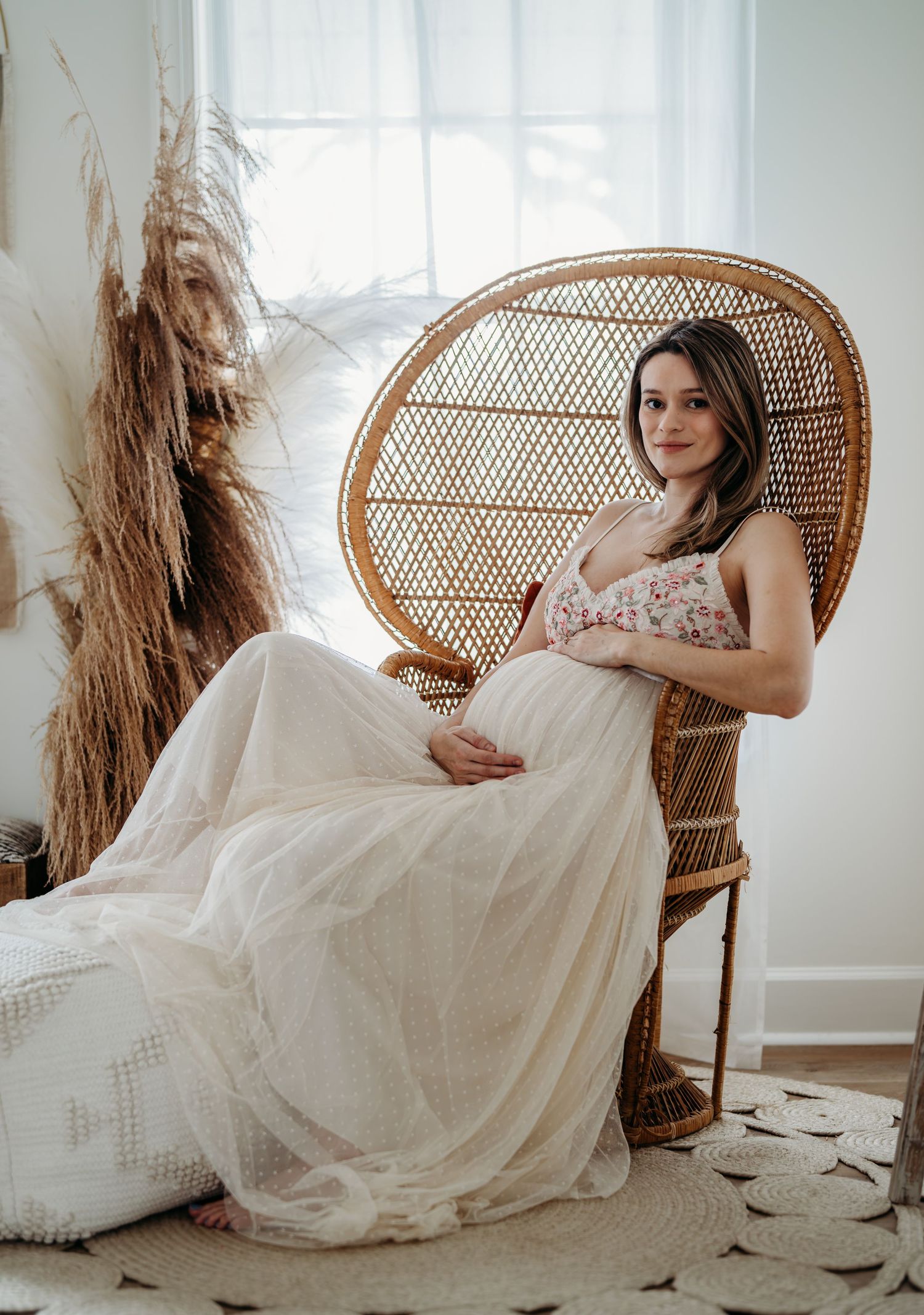 Dreamy maternity photo with peacock chair and soft tulle dress in natural light with pampas grass decor.
