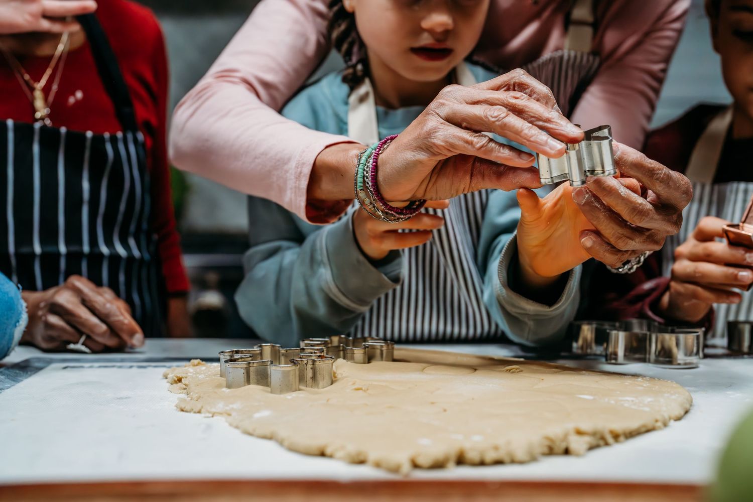 Hands roll out dough on a wooden surface with measuring cups and baking ingredients nearby.