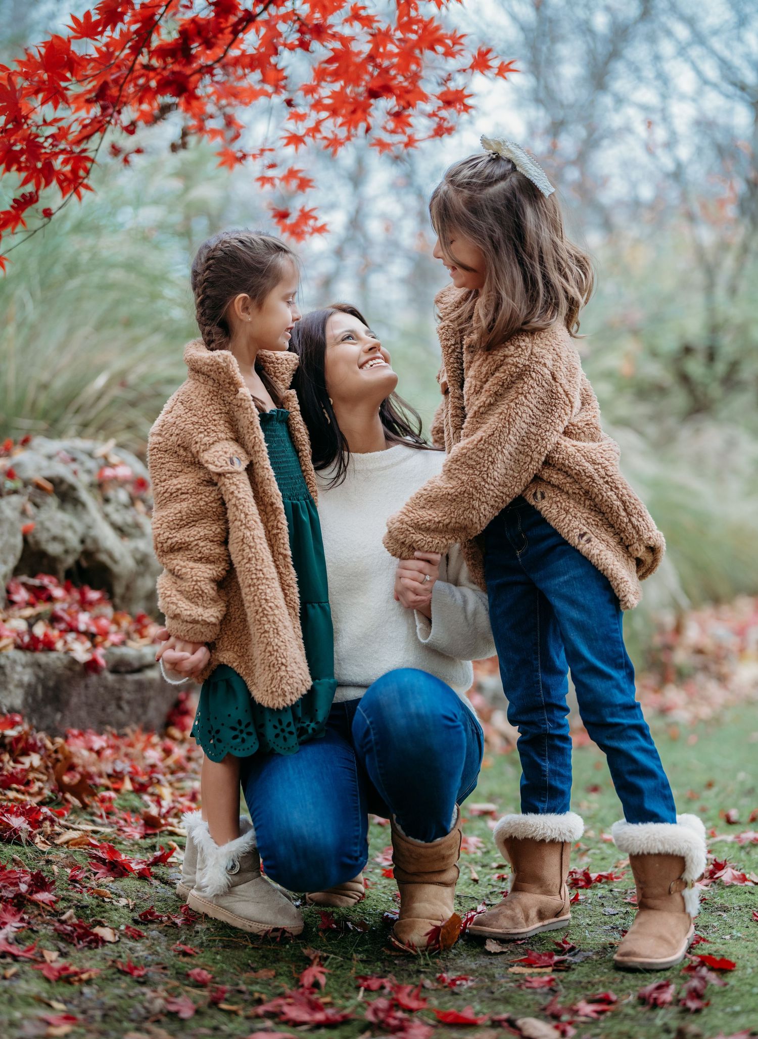 A tender family moment captured under vibrant red autumn leaves with cozy teddy bear jackets and boots in nature.