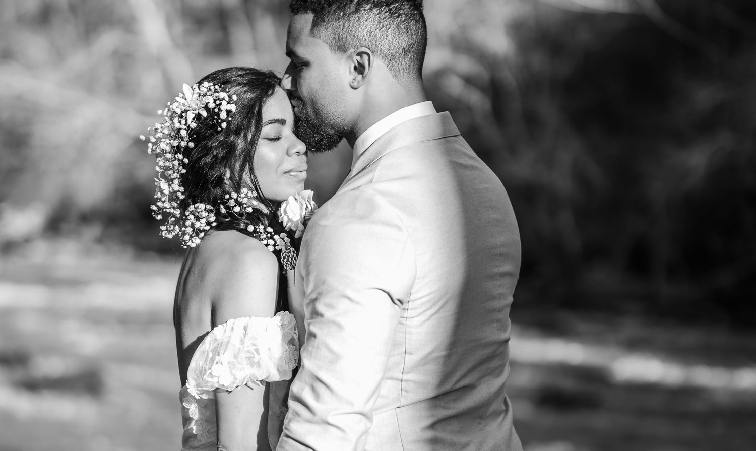 A romantic black and white wedding portrait shows a tender moment between newlyweds, with the bride wearing a floral crown.