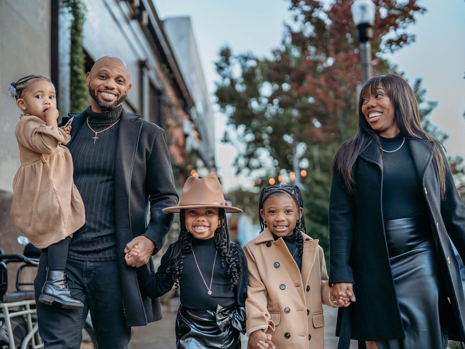 Family wearing winter coats walks together outdoors while sharing joyful moments in urban setting.