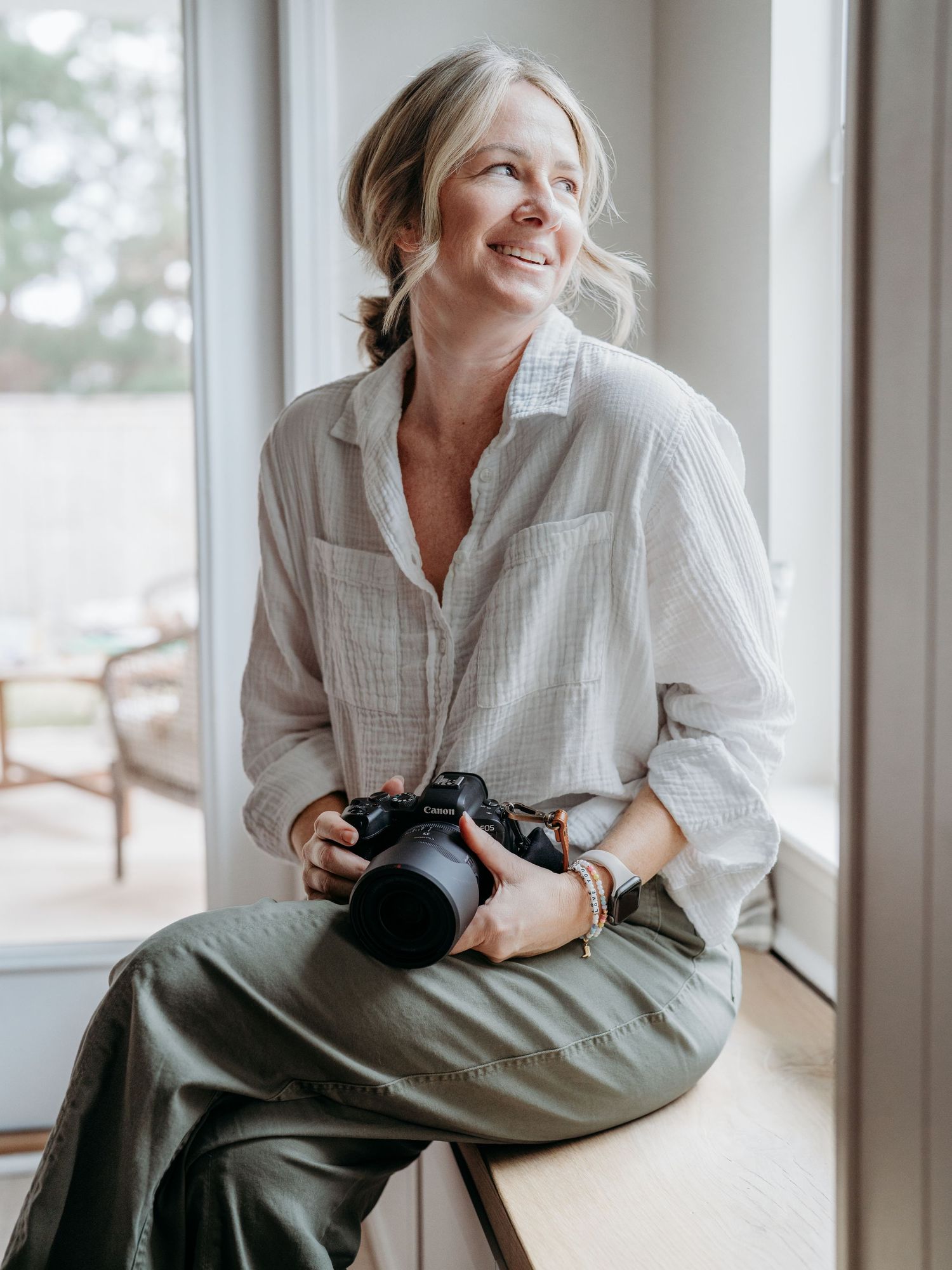 A person in a white shirt sits casually by a window with a camera, shown in a series of relaxed poses.