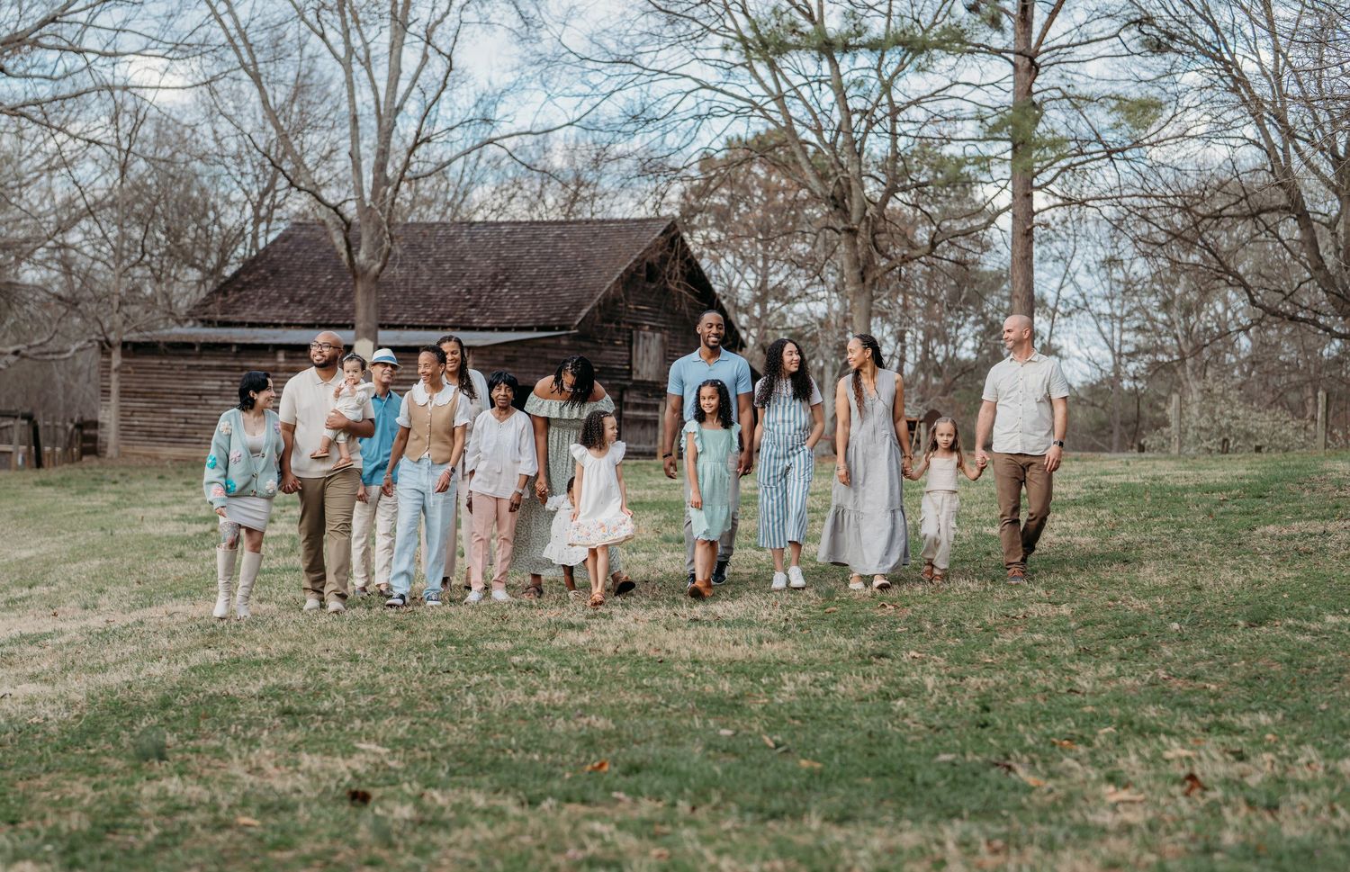 A group in coordinated light blue and white outfits walks together on grass near a rustic wooden cabin in springtime.