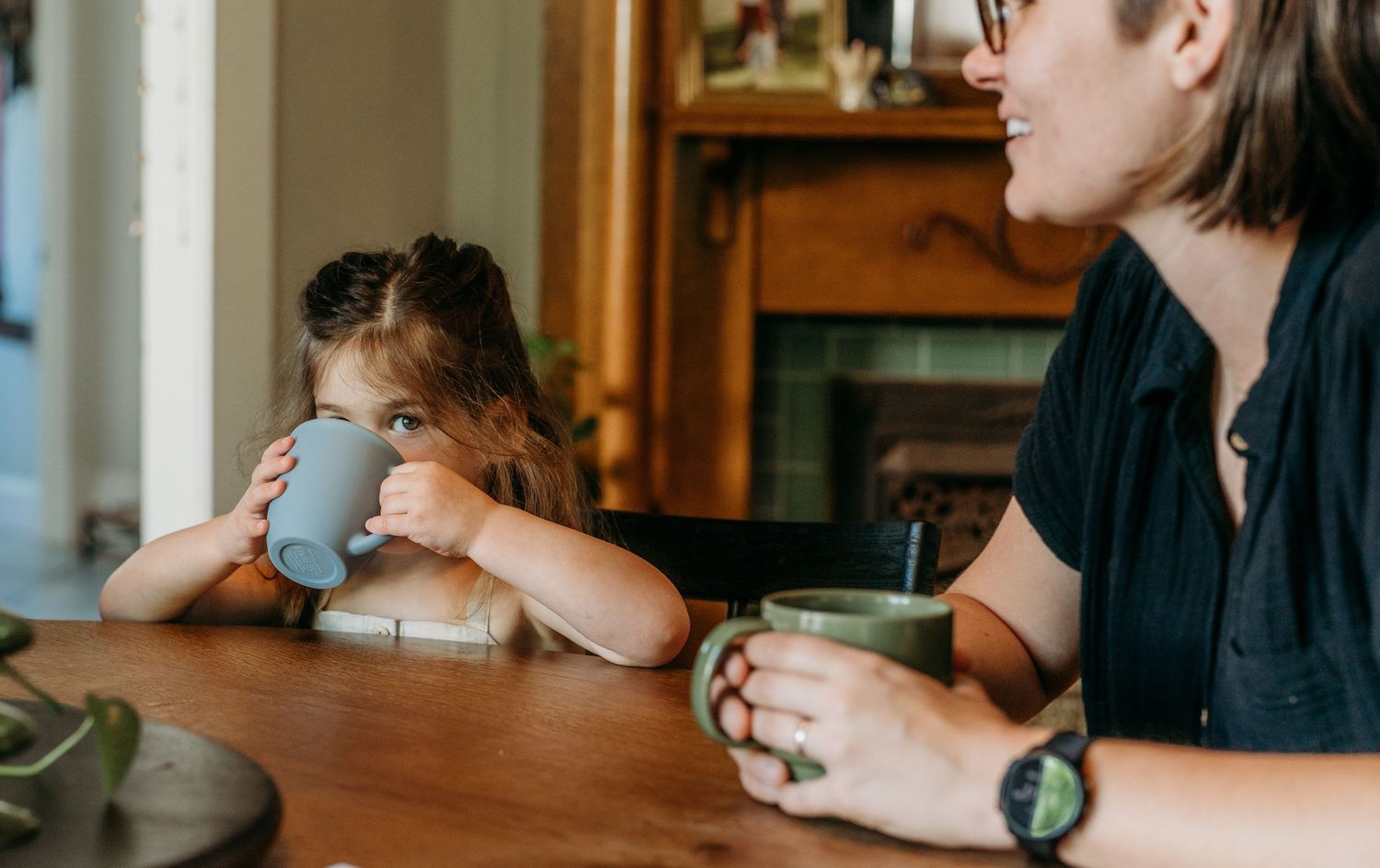 A young child and adult sit at a wooden table in a cozy interior setting while having a conversation over drinks.
