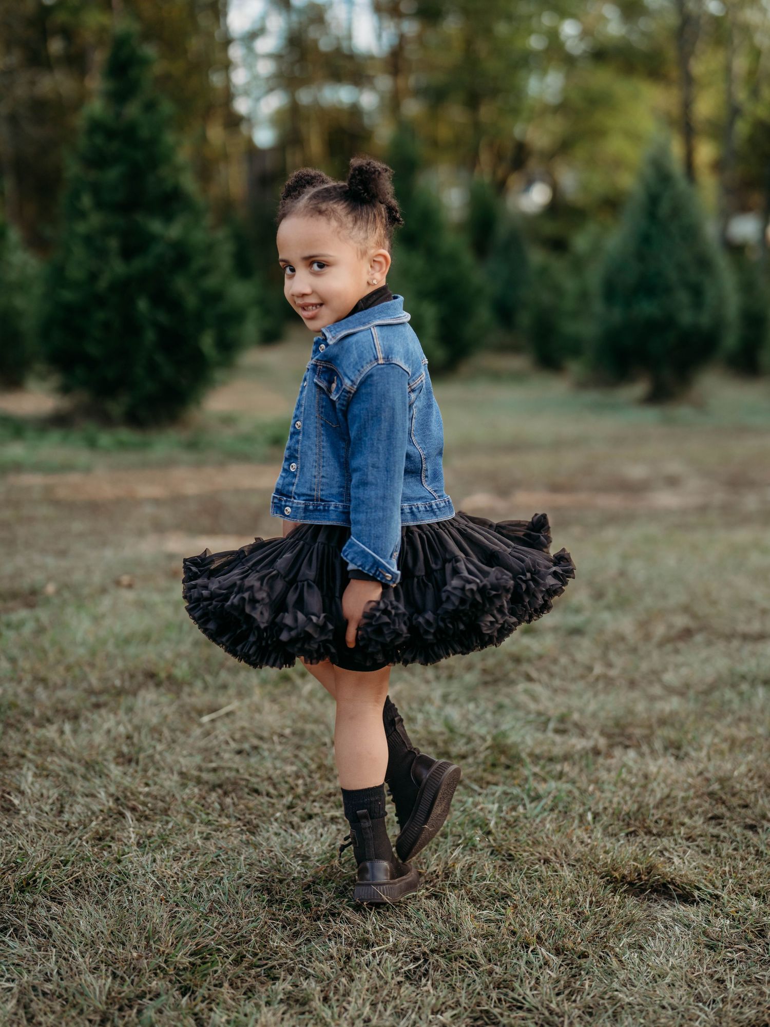 A young dancer in a denim jacket and black tutu twirls playfully in a grassy field during autumn.