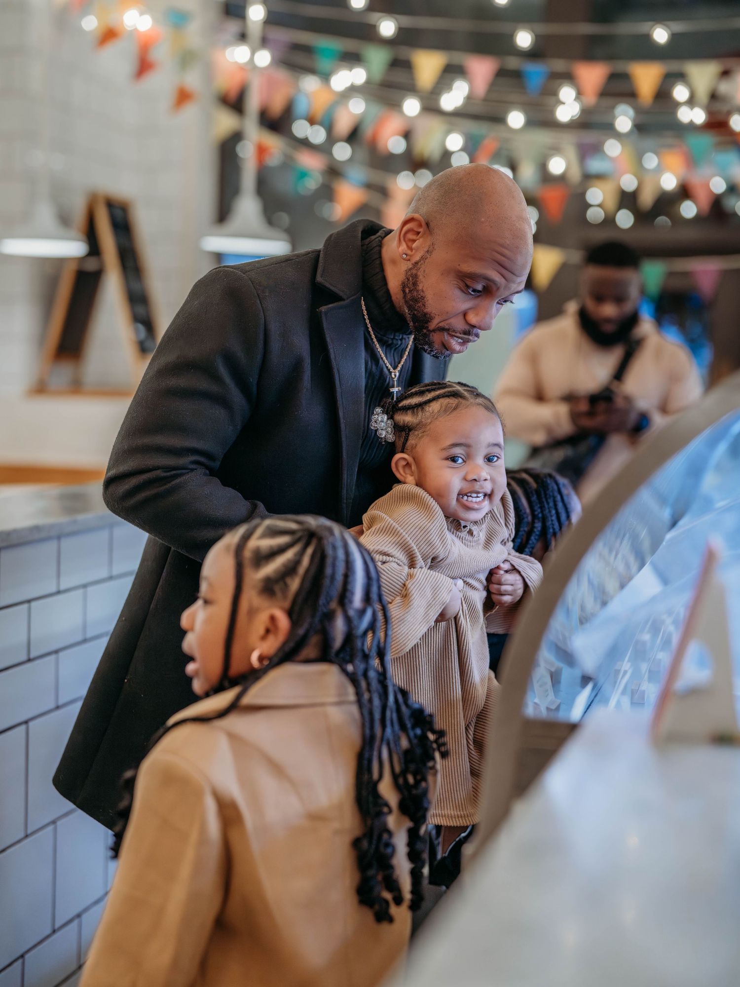 A tender moment shared between a dad and his daughters at an ice cream parlor with festive lights.