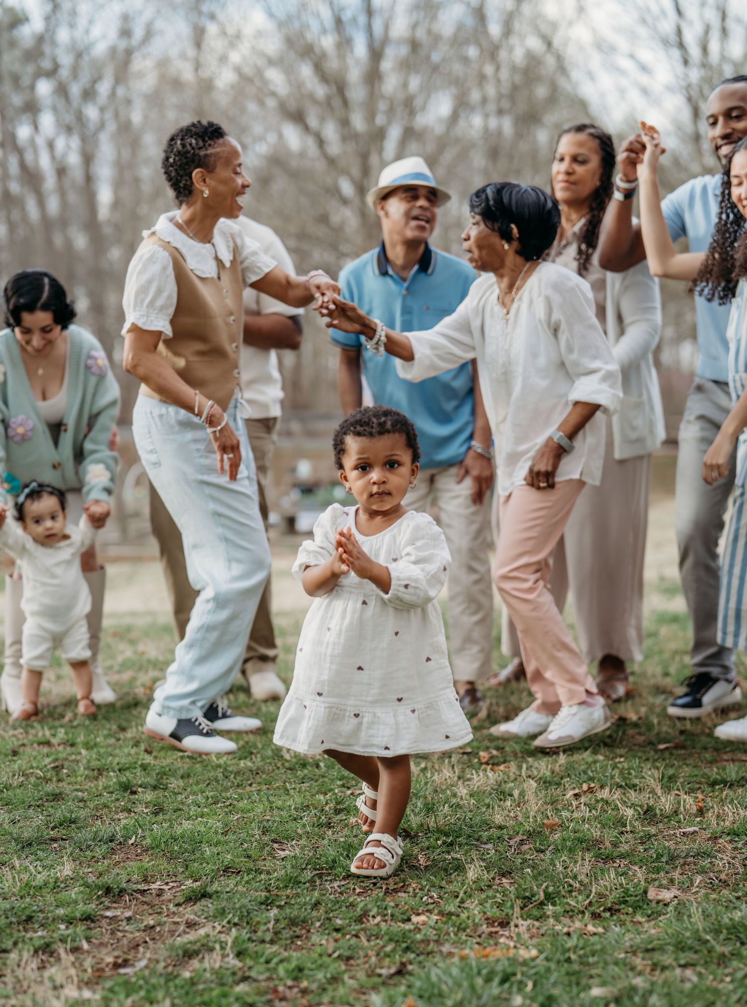 A group of people in light colored outfits dancing and celebrating together on a grassy hillside during springtime.