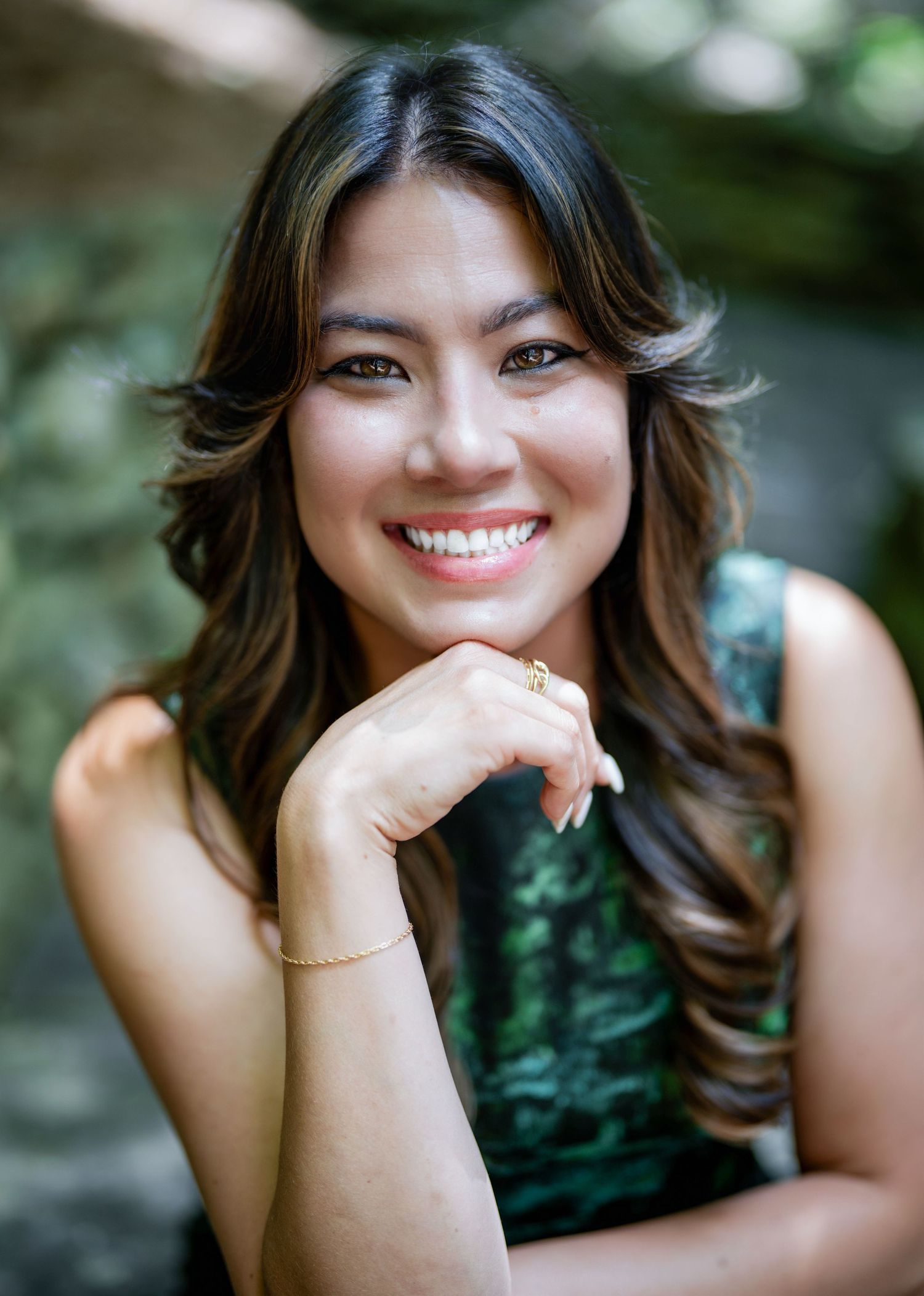 A person wearing a dark green sleeveless top poses with a warm smile against a soft blurred background.
