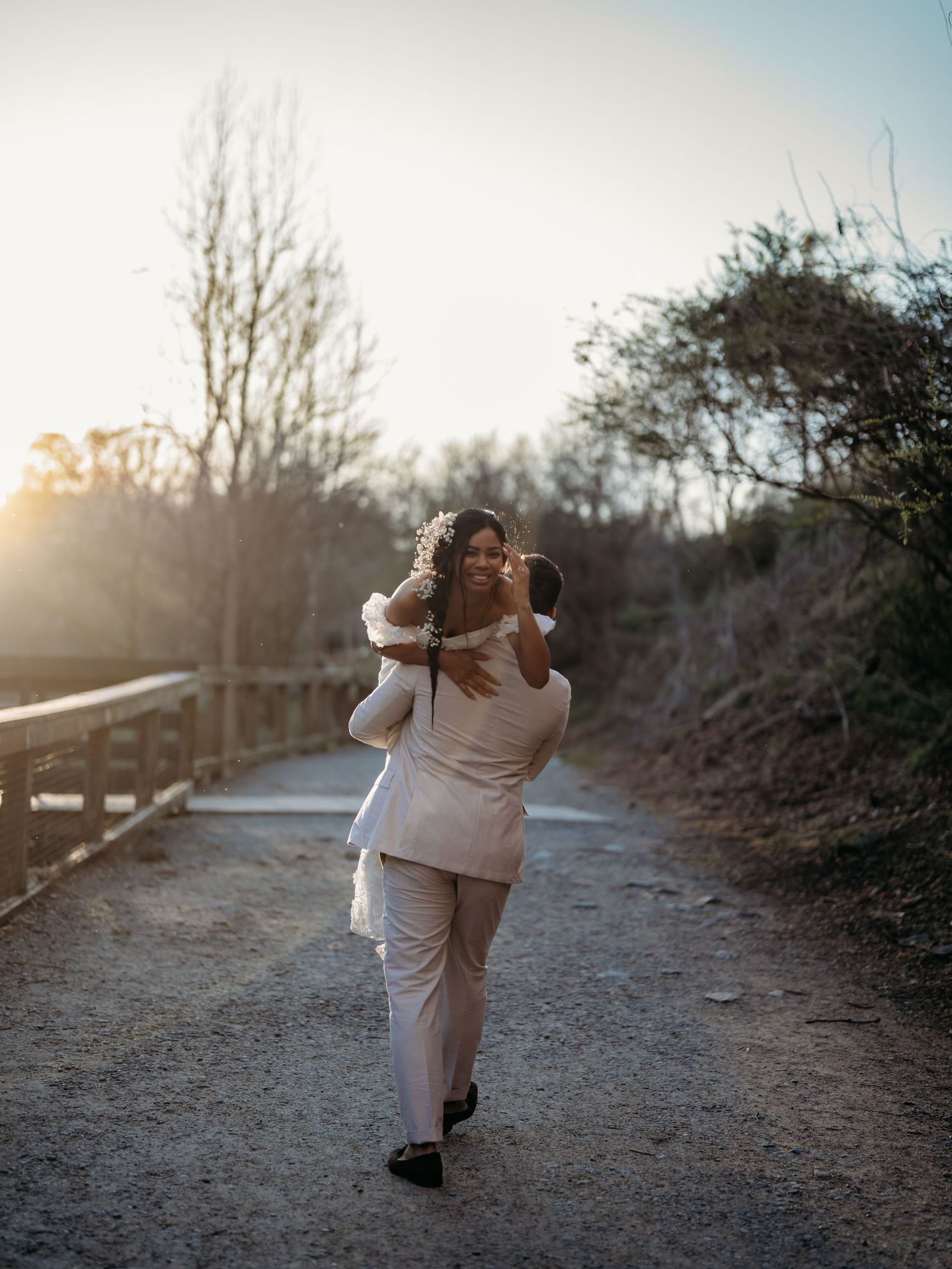 Two people sharing a tender moment on a nature path during golden hour with sun flare in the background.
