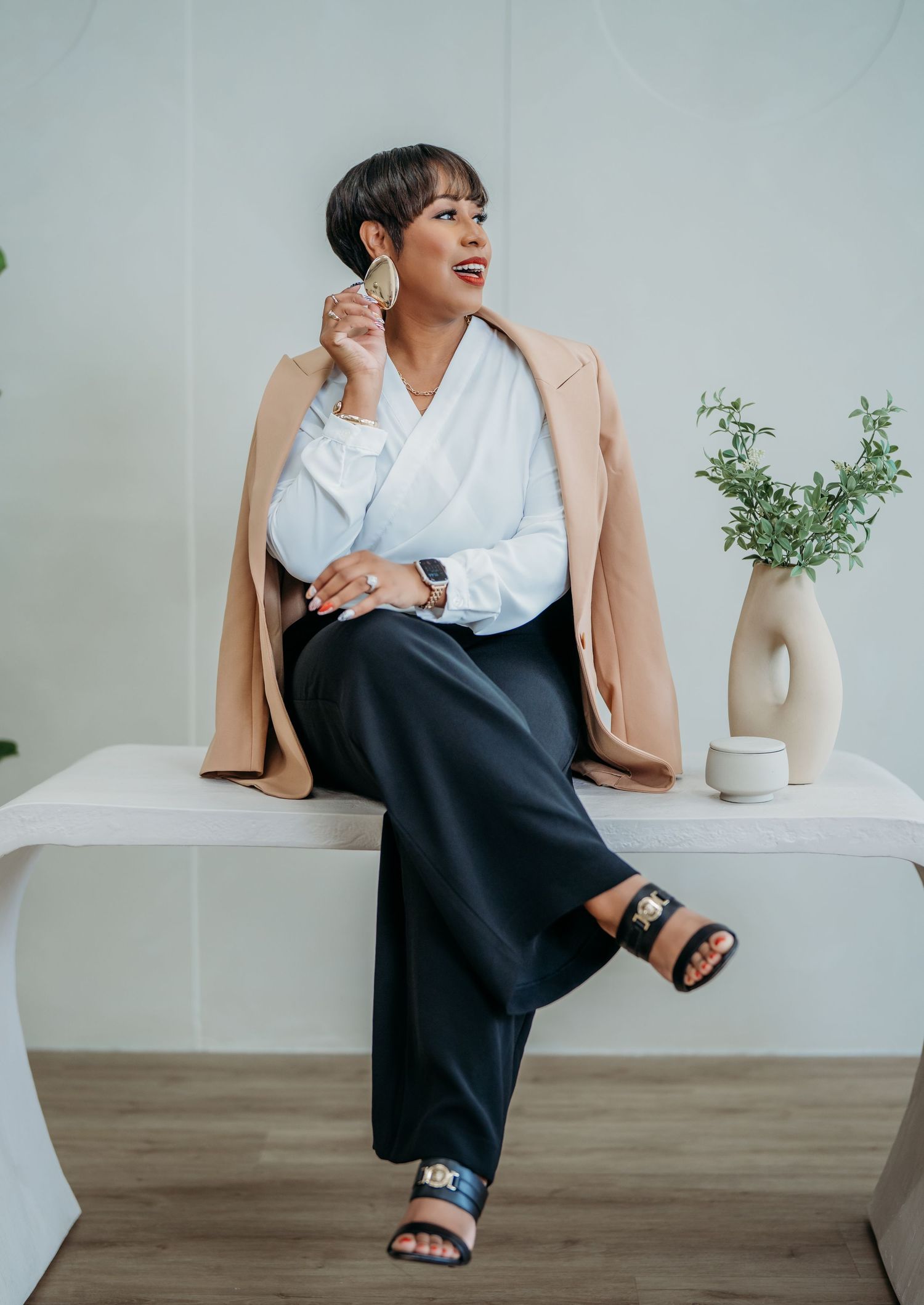 Professional smart casual outfit featuring beige coat, white button down shirt and black pants with sandals in minimalist setting.