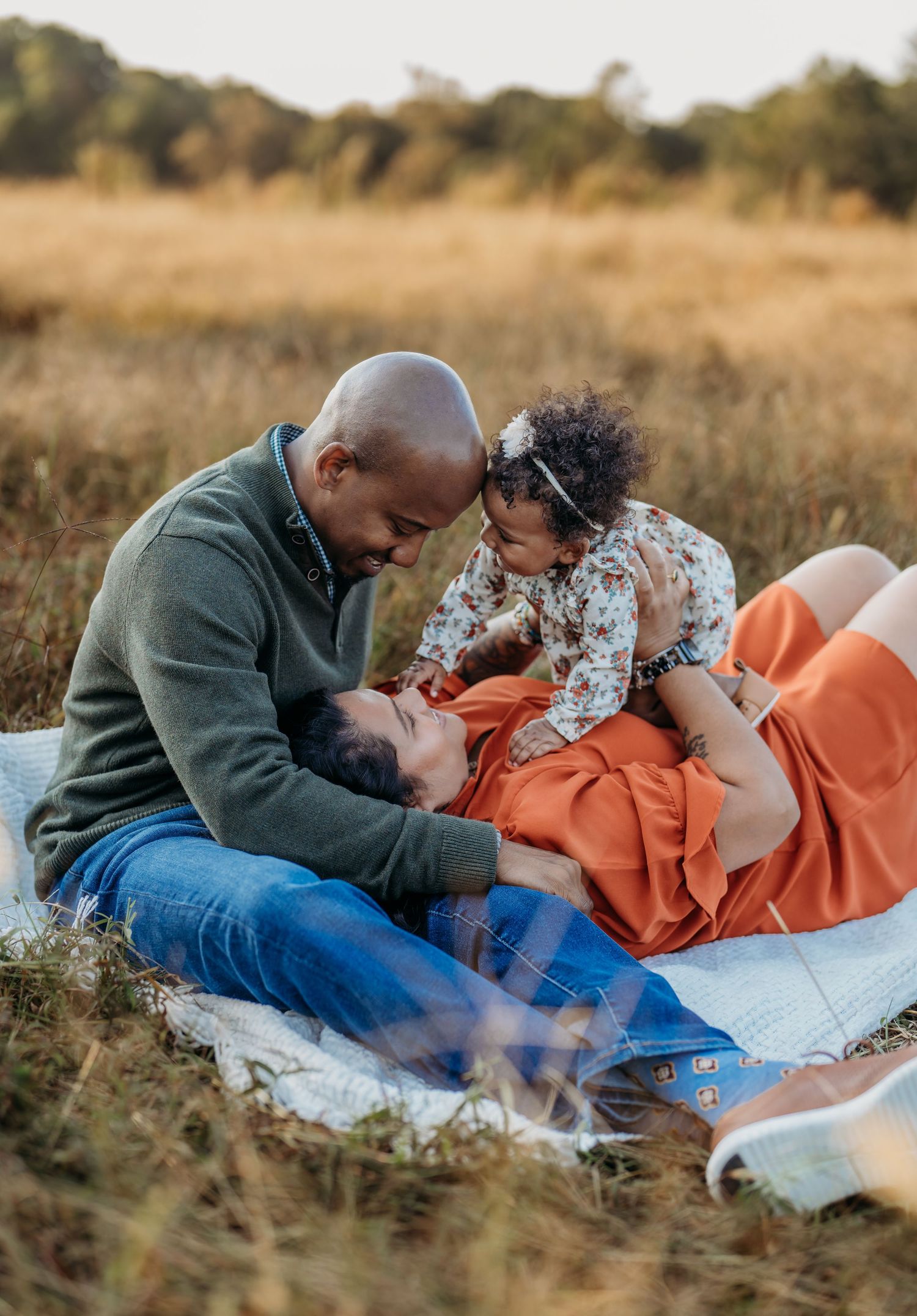 Family enjoying a tender moment together while relaxing on a picnic blanket in a golden field during sunset.