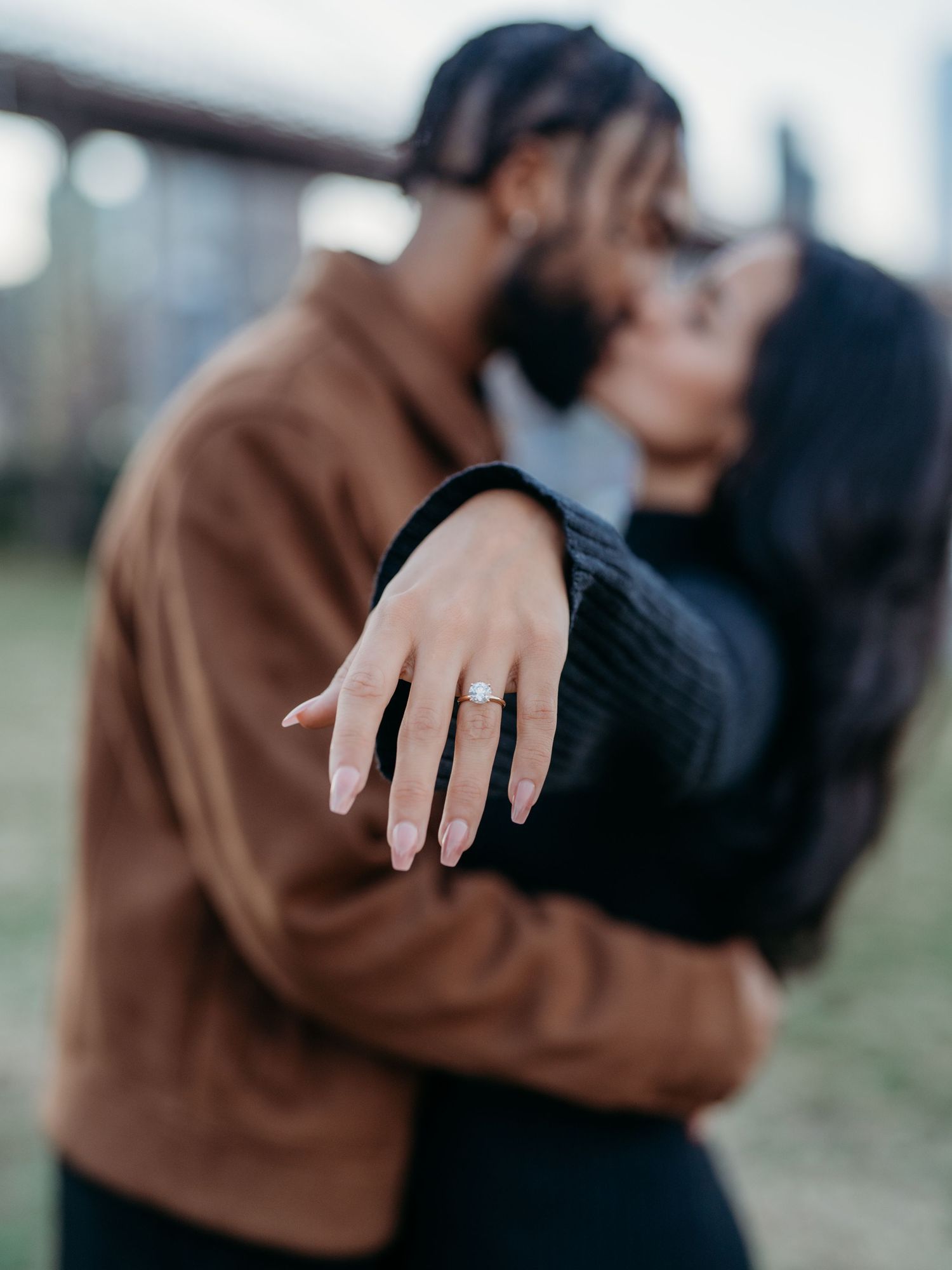 A couple sharing a romantic moment while showing off an engagement ring on a raised hand.