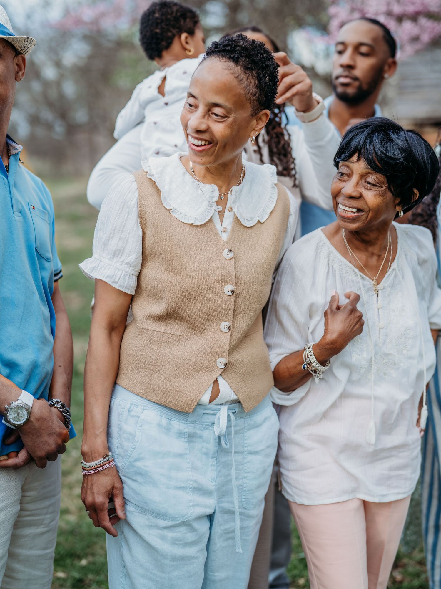A joyful group wearing light colored casual outfits laughs together outdoors during a spring gathering.