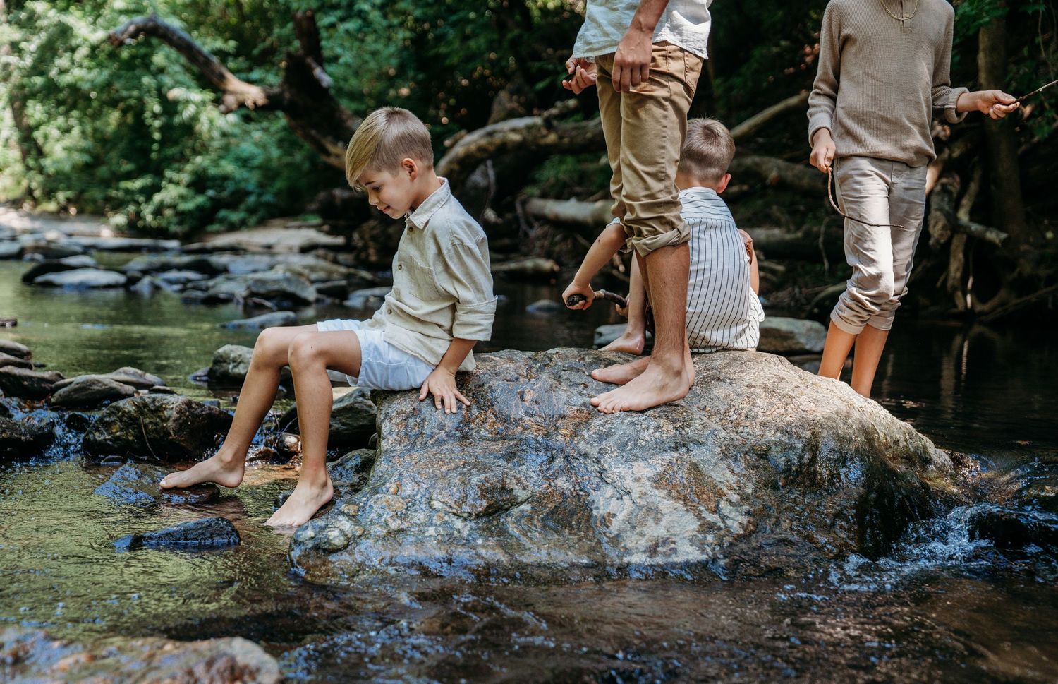 People enjoying a summer day splashing and playing in a shallow creek among rocks and trees.