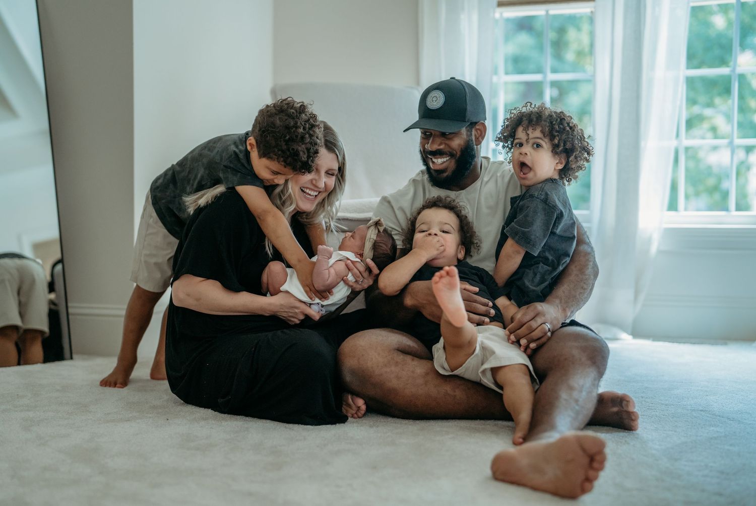 A family shares a playful moment together while sitting on the carpet of their bright, sunlit living room.