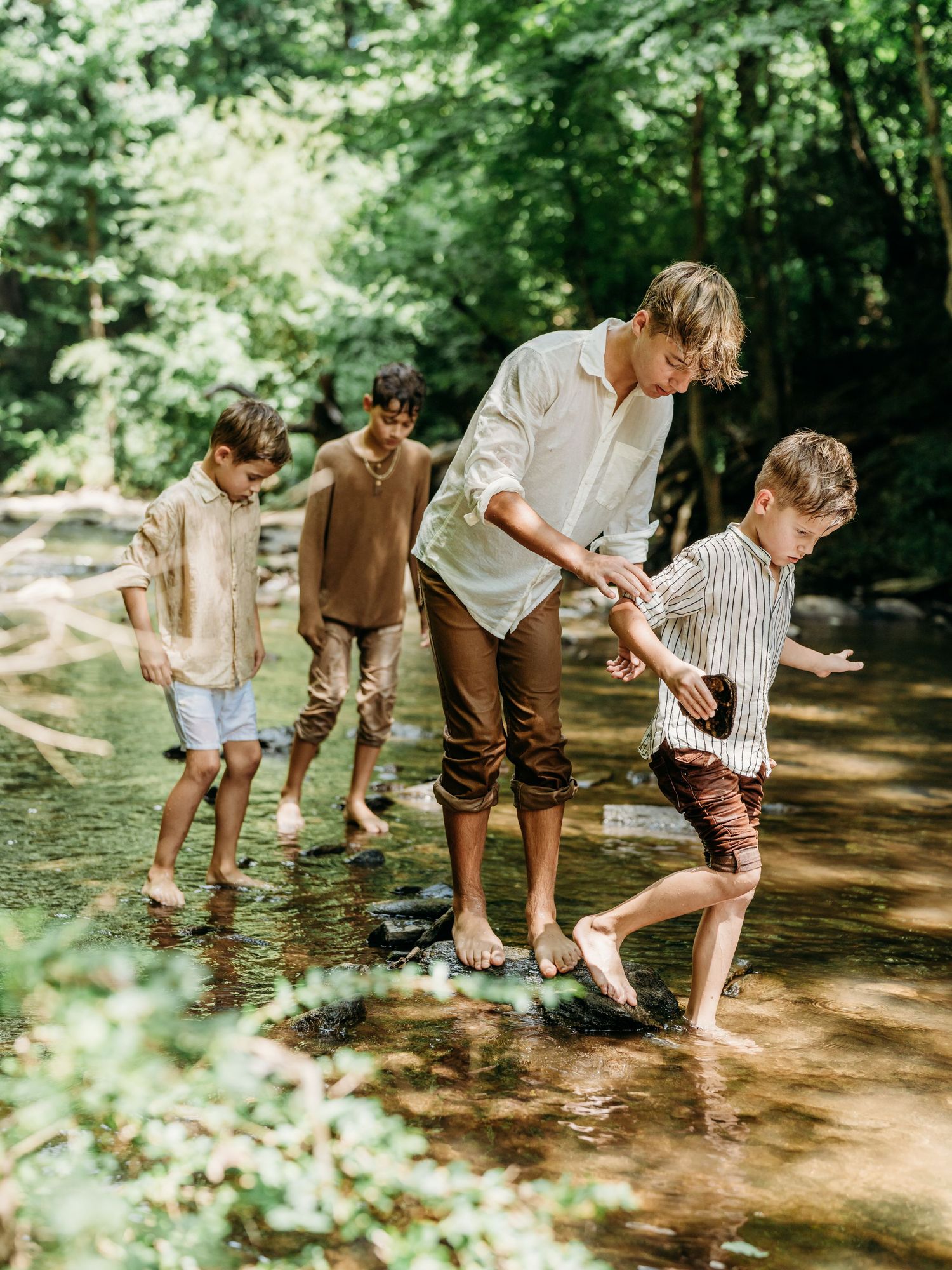 Children splash and play together in a shallow creek on a sunny summer day in the forest.