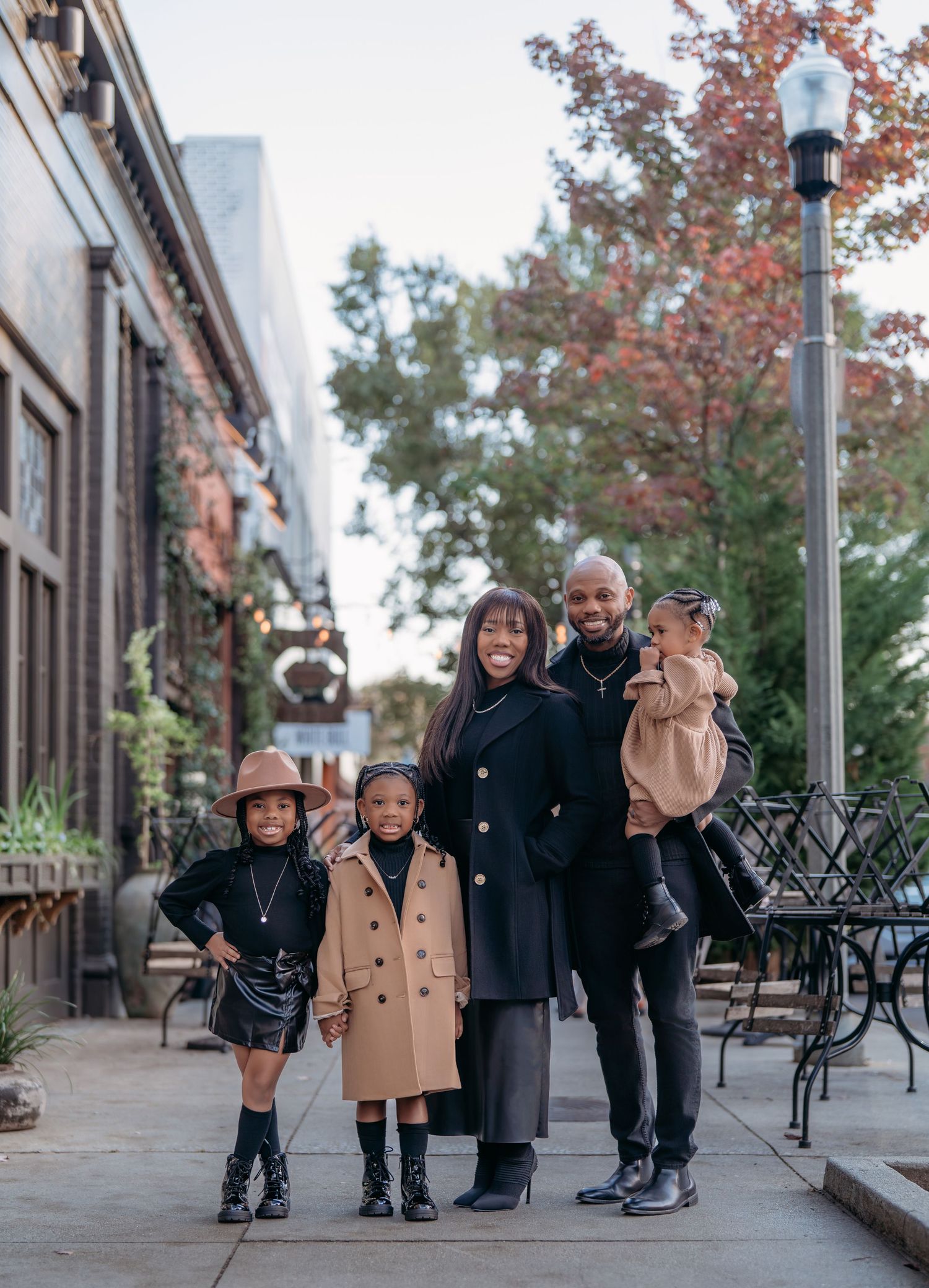 An African American young family walks together on an urban sidewalk during autumn with fall foliage visible in the trees.