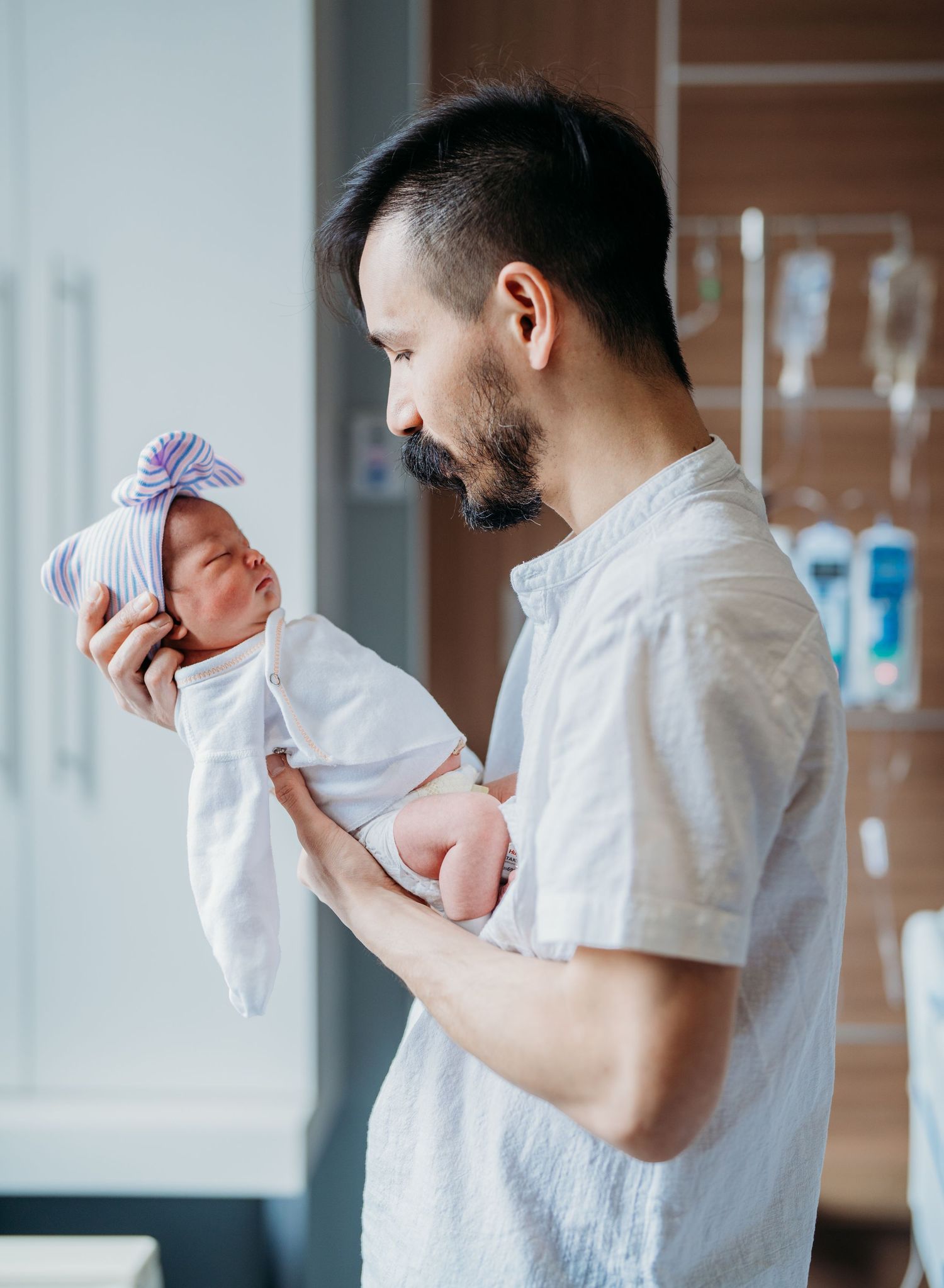 A father in a white shirt holds and kisses his newborn baby in a series of tender moments.