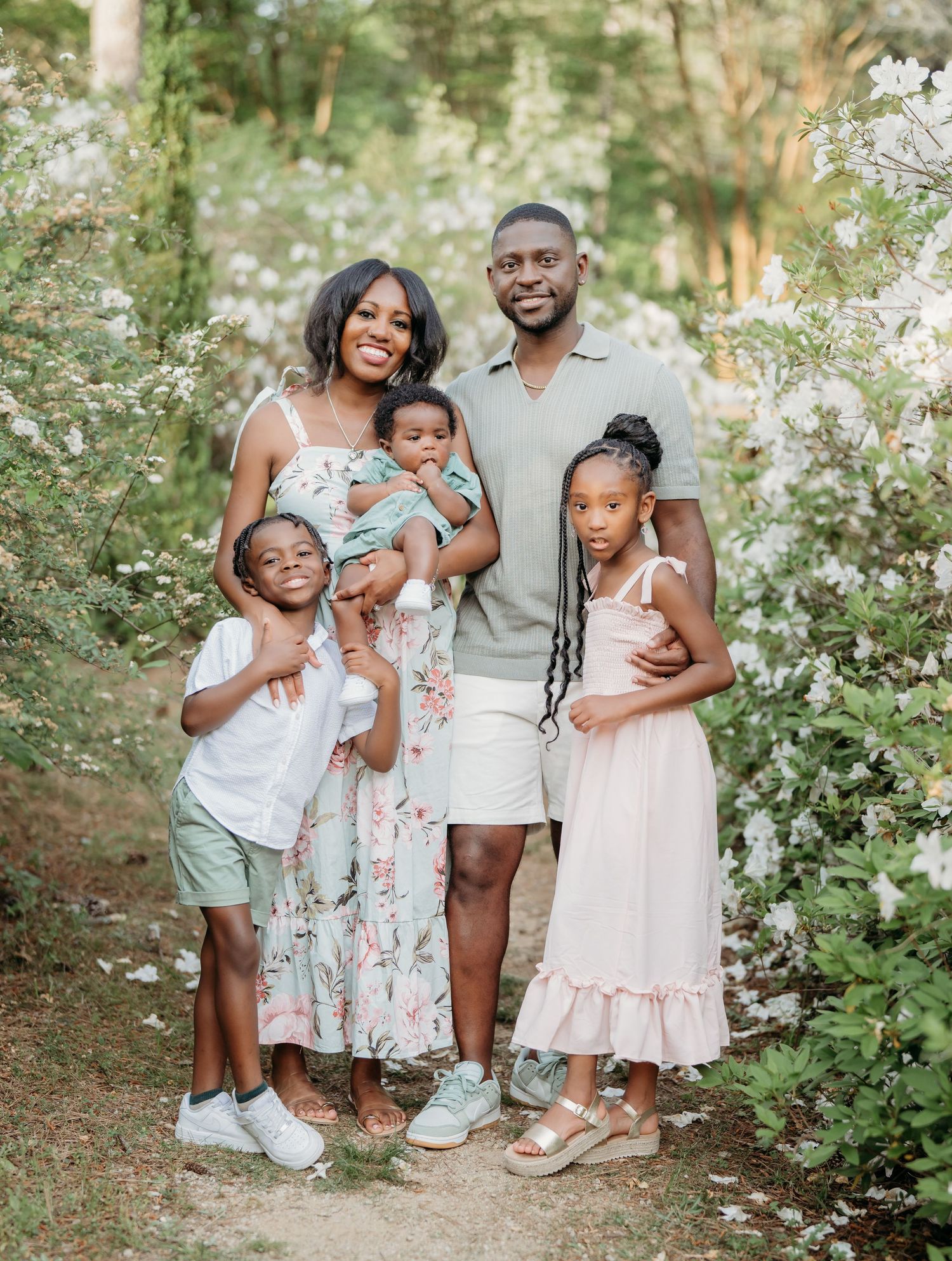 A happy family poses together in a garden setting surrounded by delicate white flowers.