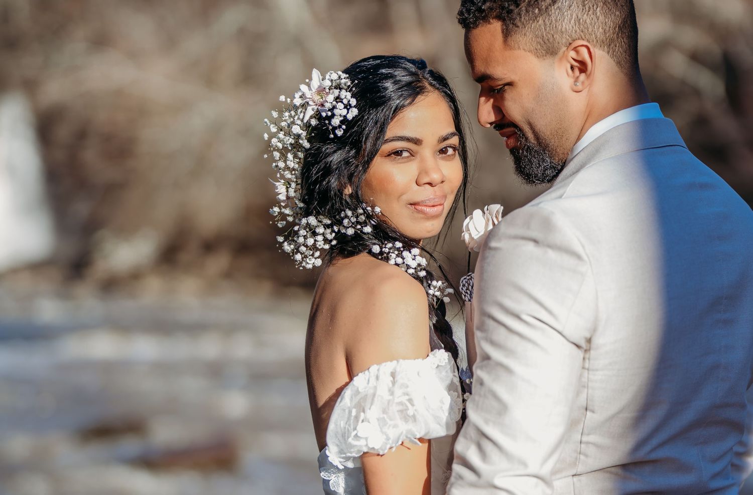 A romantic wedding couple shares an intimate moment outdoors, with the bride wearing a delicate floral crown and off-shoulder dress.