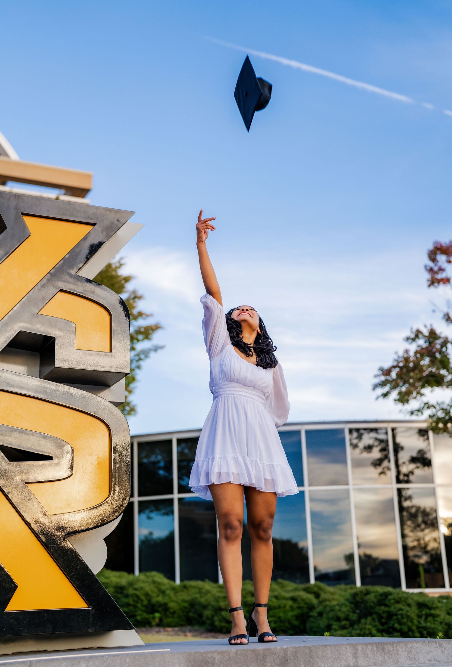 A dancer in a white dress performs graceful leaps and poses against a blue sky backdrop with modern architecture.