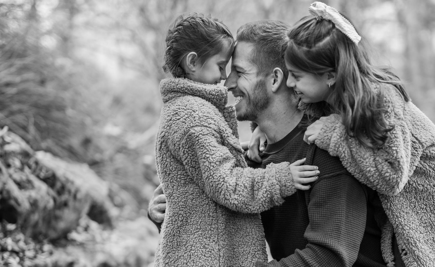 Black and white portrait of a family sharing an intimate moment outdoors while wearing cozy sweaters.