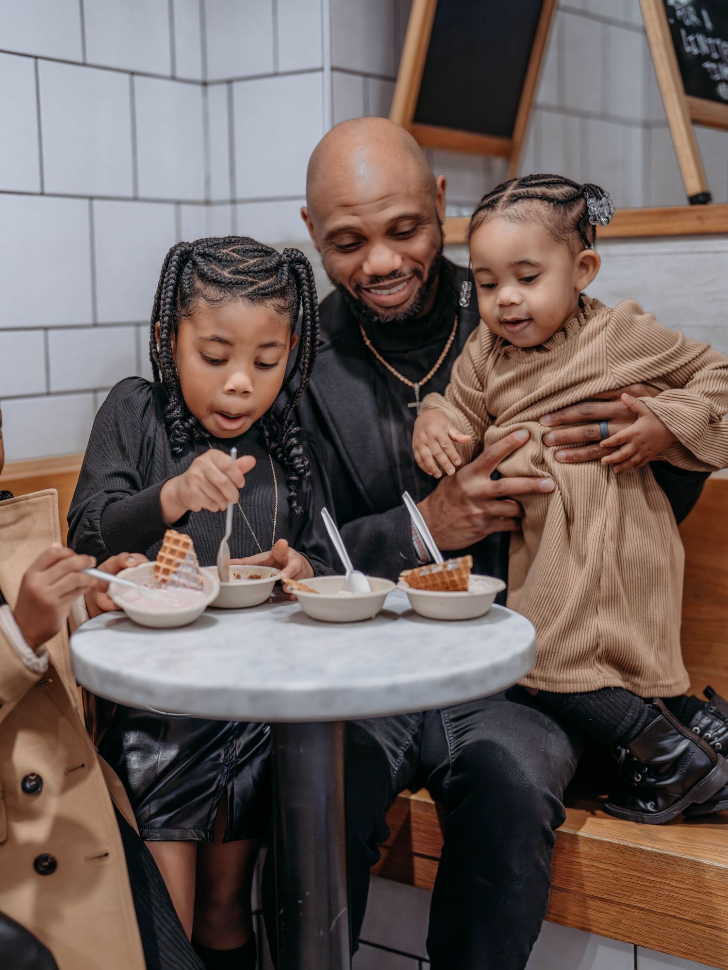 A dad and his two small daughters, enjoying Ice Cream at Jeni's Ice Cream Shope at a small cafe table. Decatur, GA