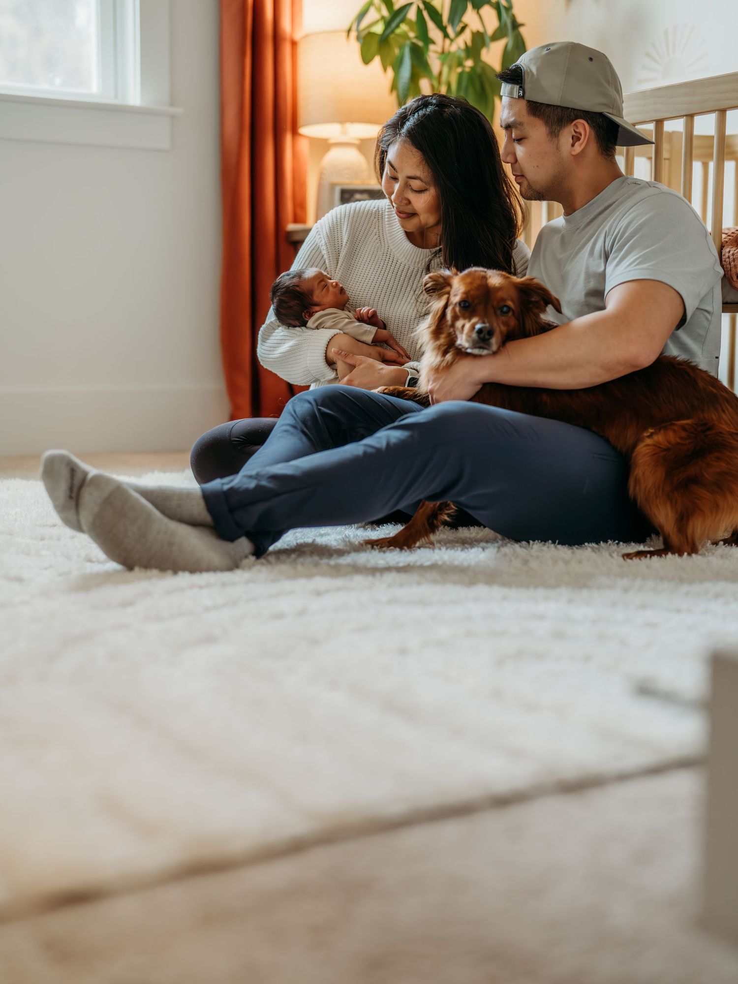 Family relaxing on plush white carpet at home with small brown dog.