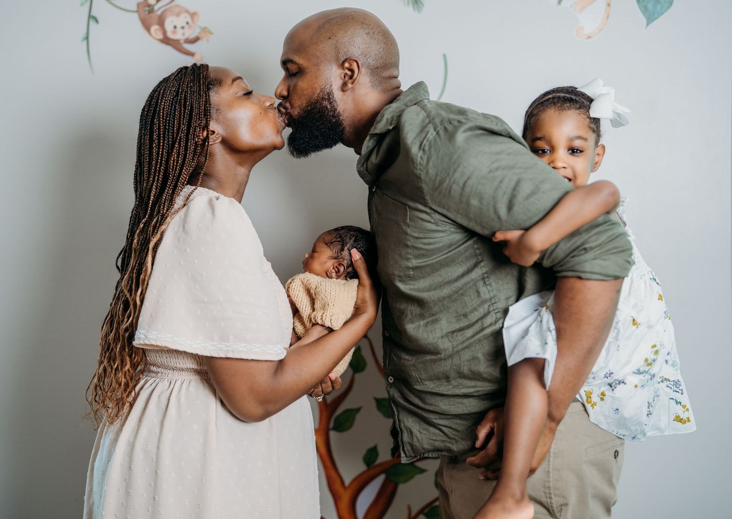Family in coordinating white and olive outfits sharing sweet candid moments against a gray wall.