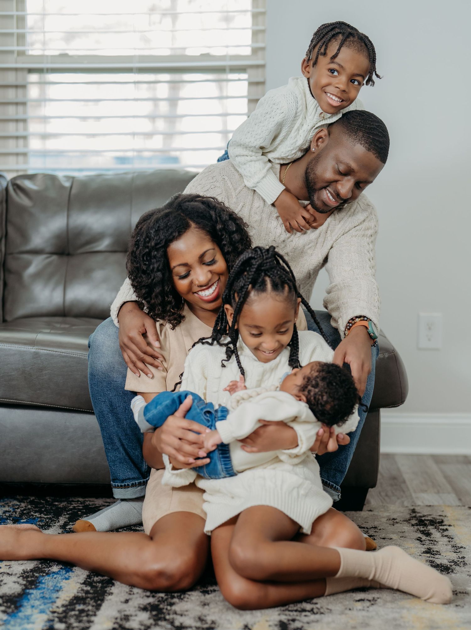 A family plays and laughs together while sitting on a patterned rug in their living room space.