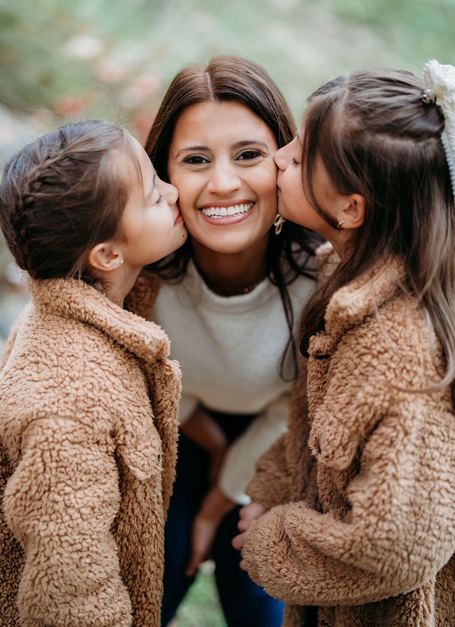 A heartwarming moment captured as two children in matching teddy bear coats share kisses and smiles outdoors.