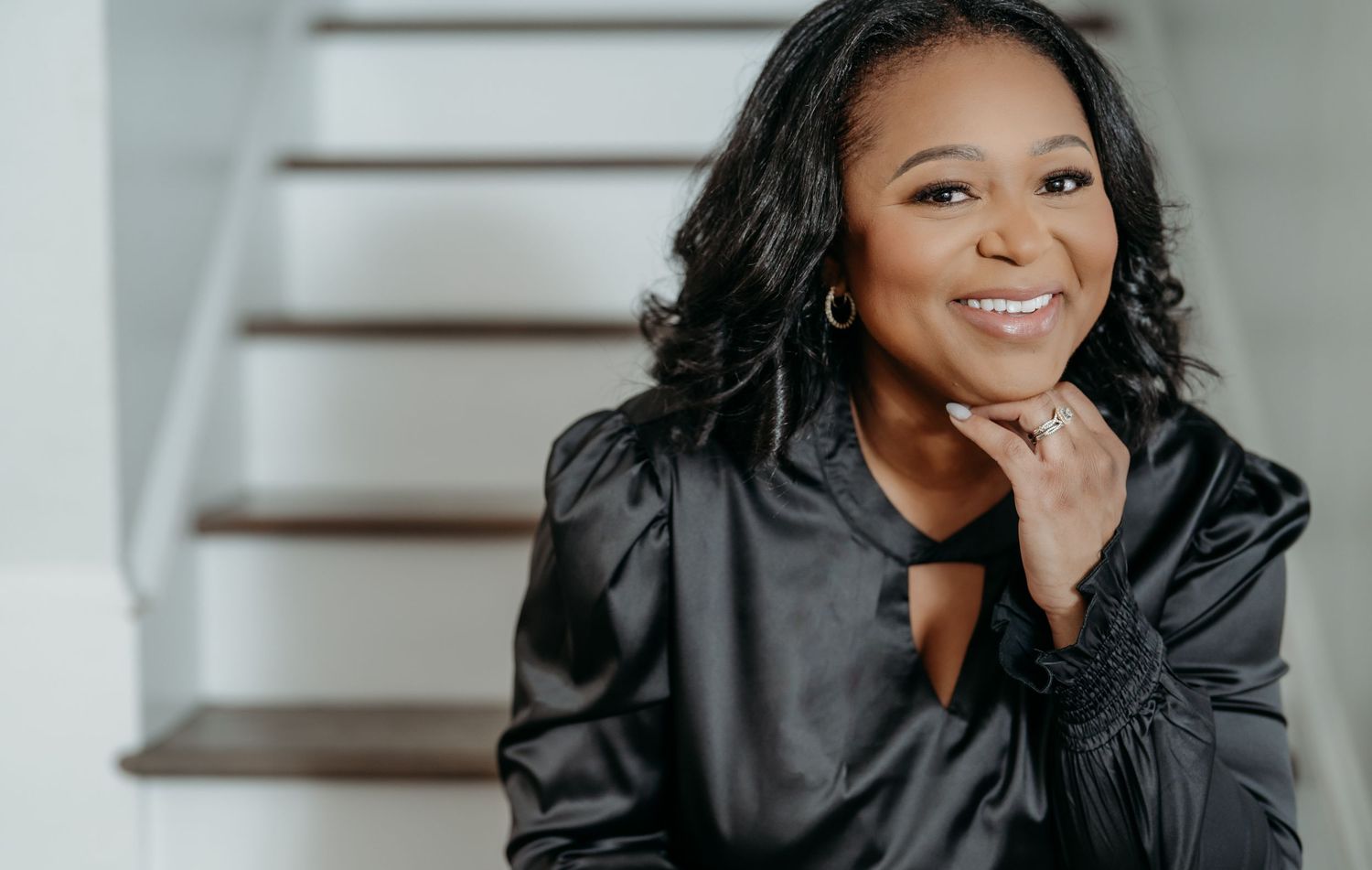 Professional headshot showing a smiling person in black leather jacket sitting on wooden stairs.