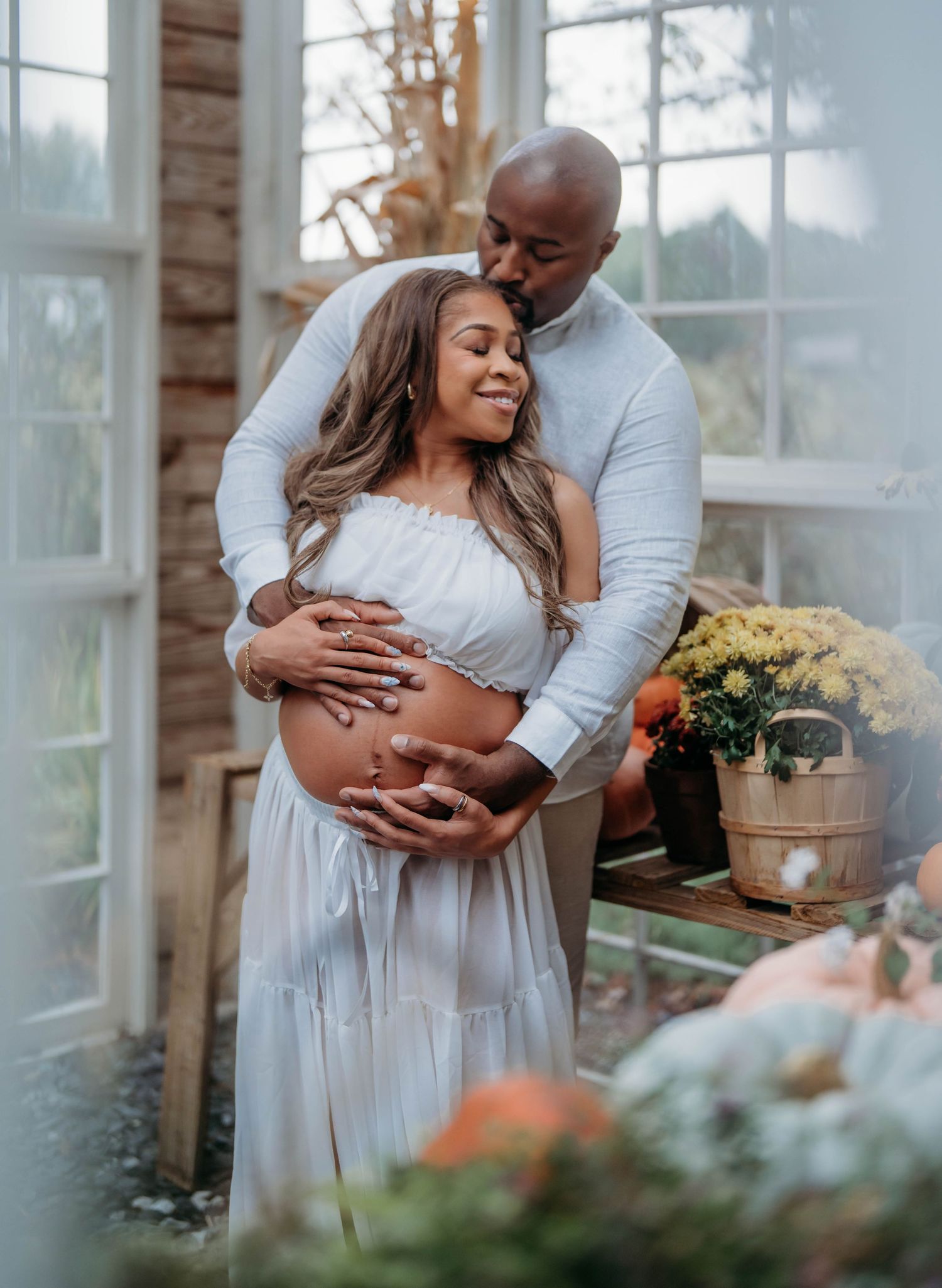 A tender embrace captured in a sunlit room with rustic decor and potted flowers.
