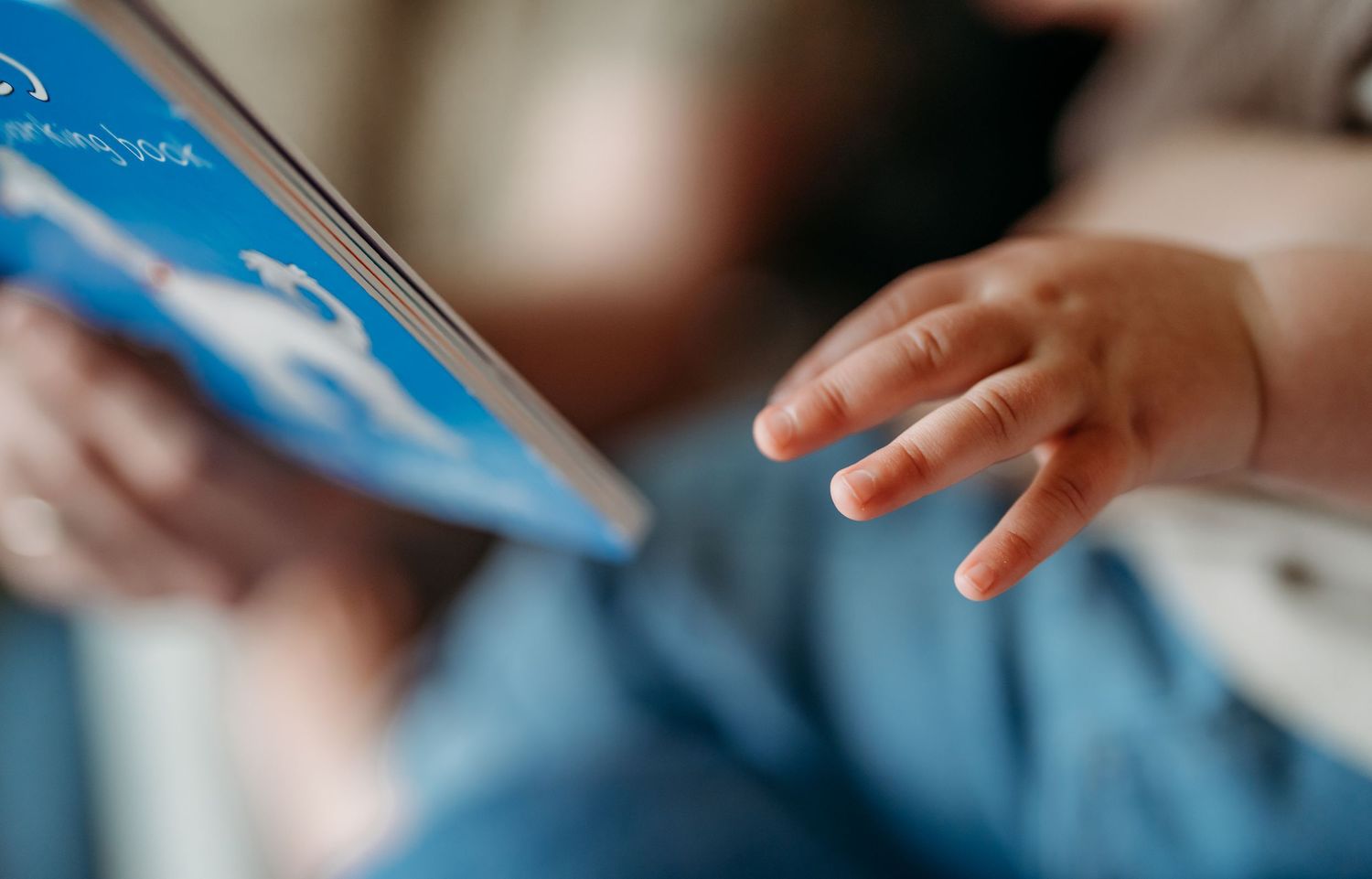 A small child's hand reaches out towards a blue book or document in a soft-focus close-up shot.