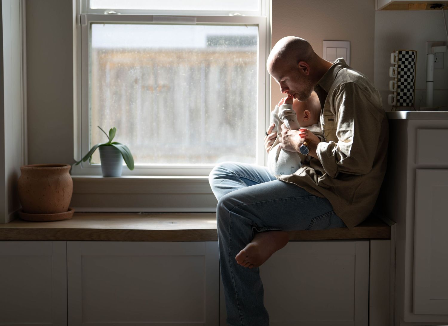A person sits alone by a window in a dimly lit room, creating a contemplative and moody atmosphere.