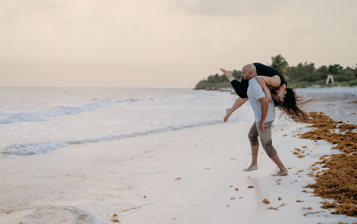 Series of similar shots showing someone bending down to examine washed up seaweed along a pristine white sand beach at sunset.